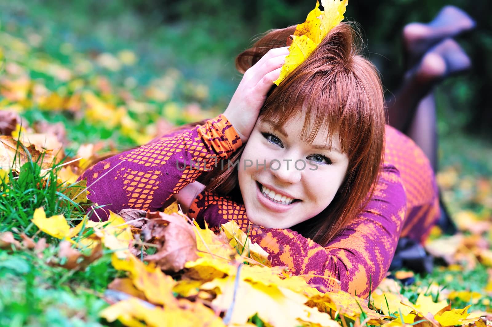 happy redheaded girl laying on the leaves in autumn forest