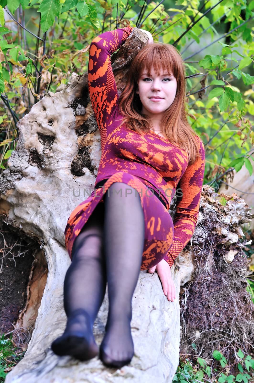 redheaded girl sitting on the log in forest 
