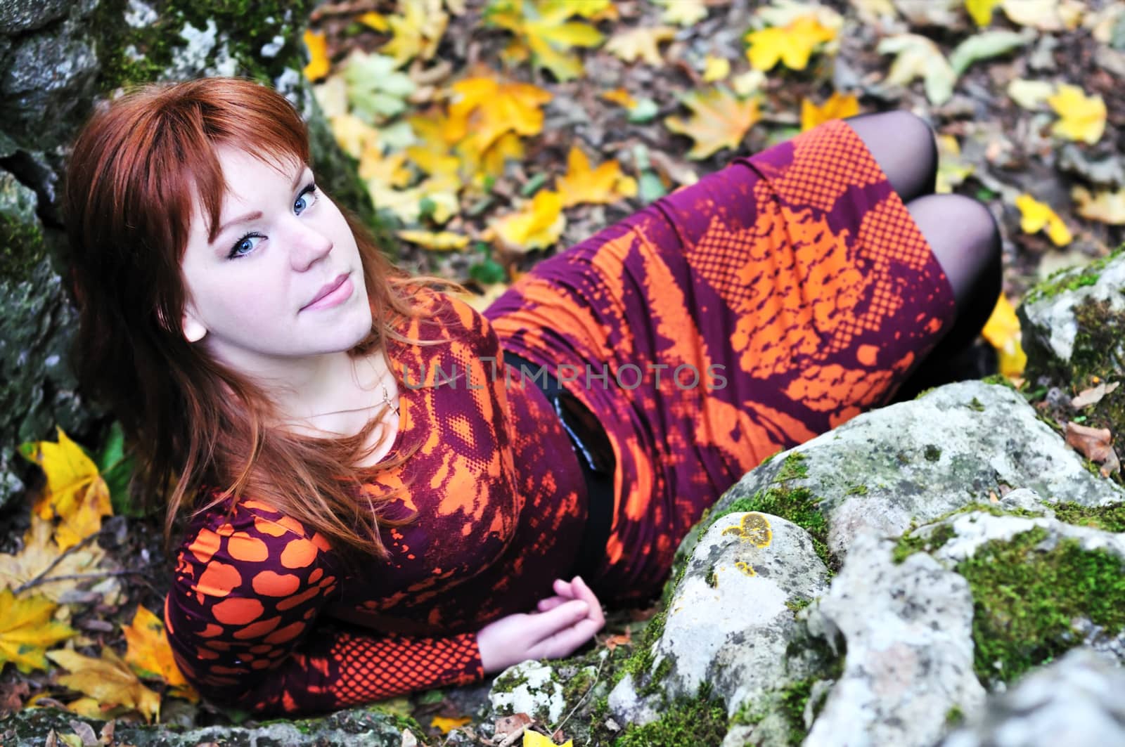 redheaded girl sitting near stones and  autumn leaves