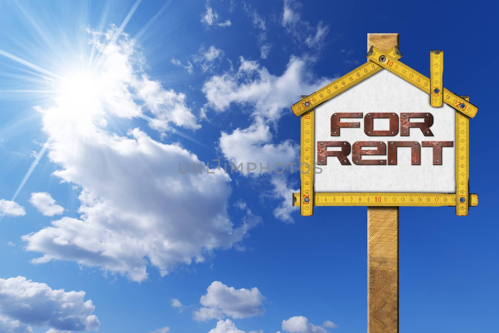 Yellow wooden meter ruler in the shape of house with text for rent. For rent real estate sign on blue sky with clouds and sun rays