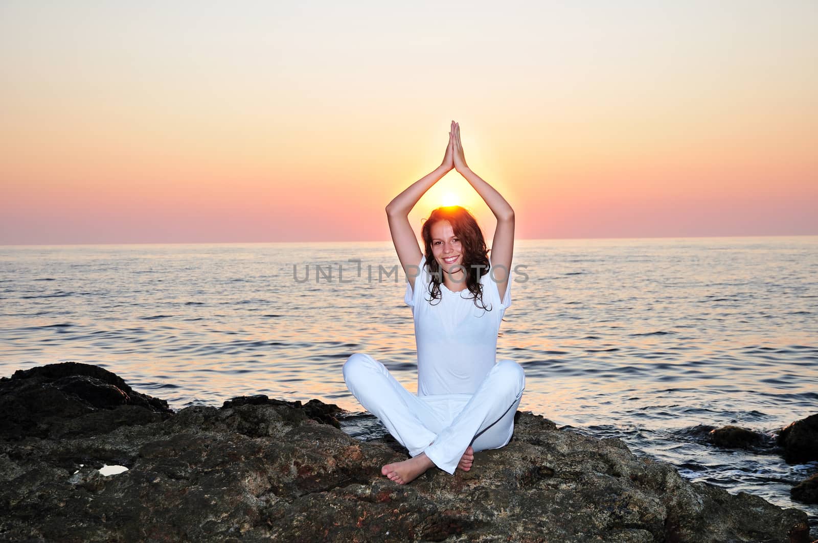 young pretty girl doing meditation on the beach in sunset time
