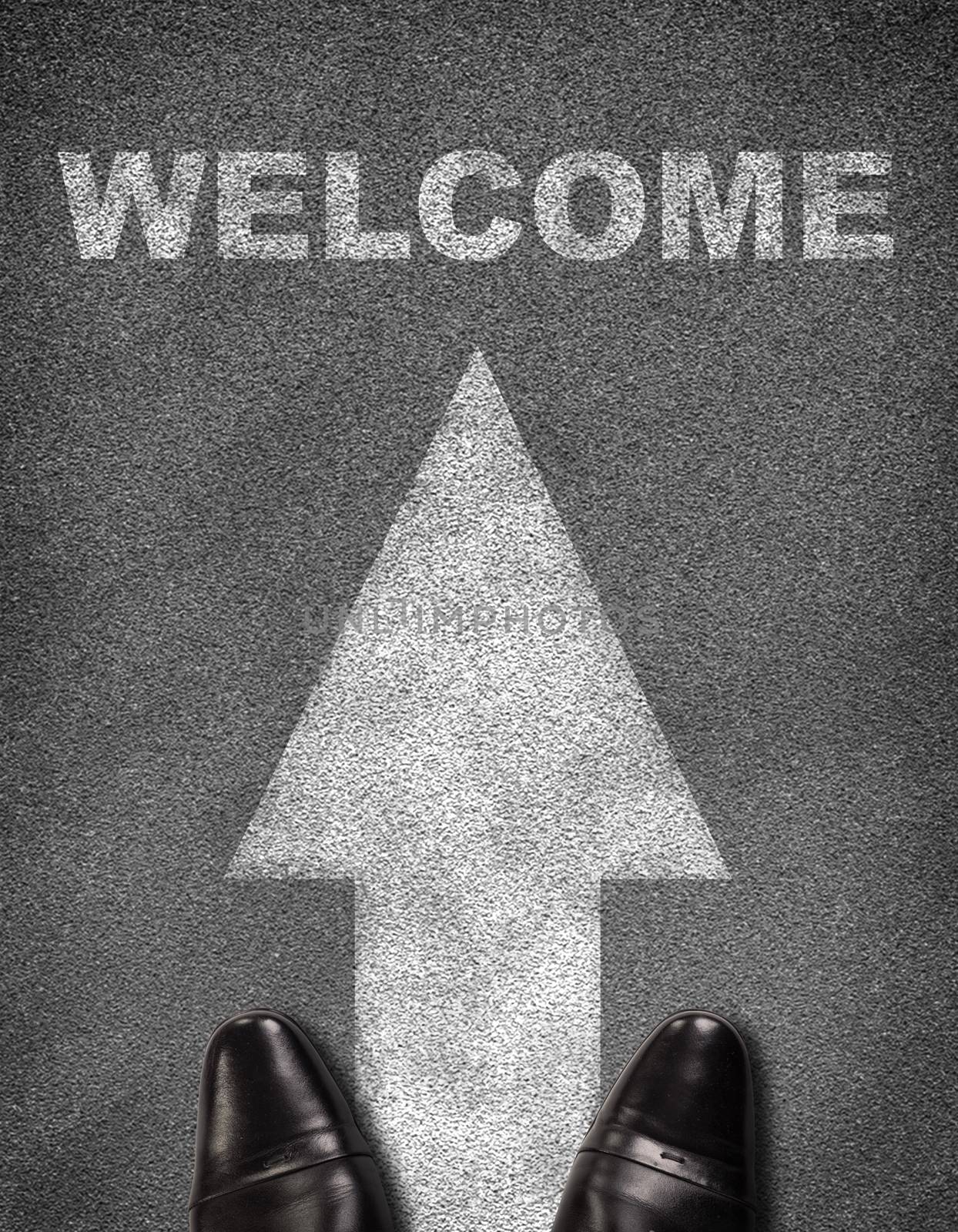 Top view of shoes standing on asphalt road with arrow and word welcome. Business concept