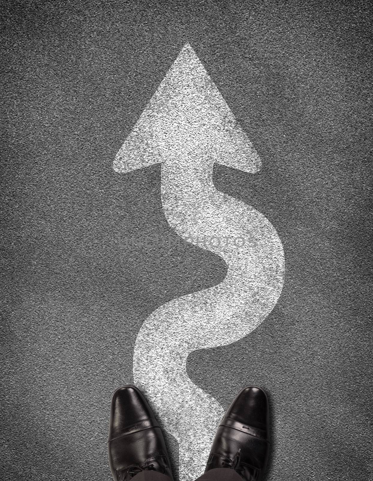 Top view of shoes standing on asphalt road with winding arrow. Business concept