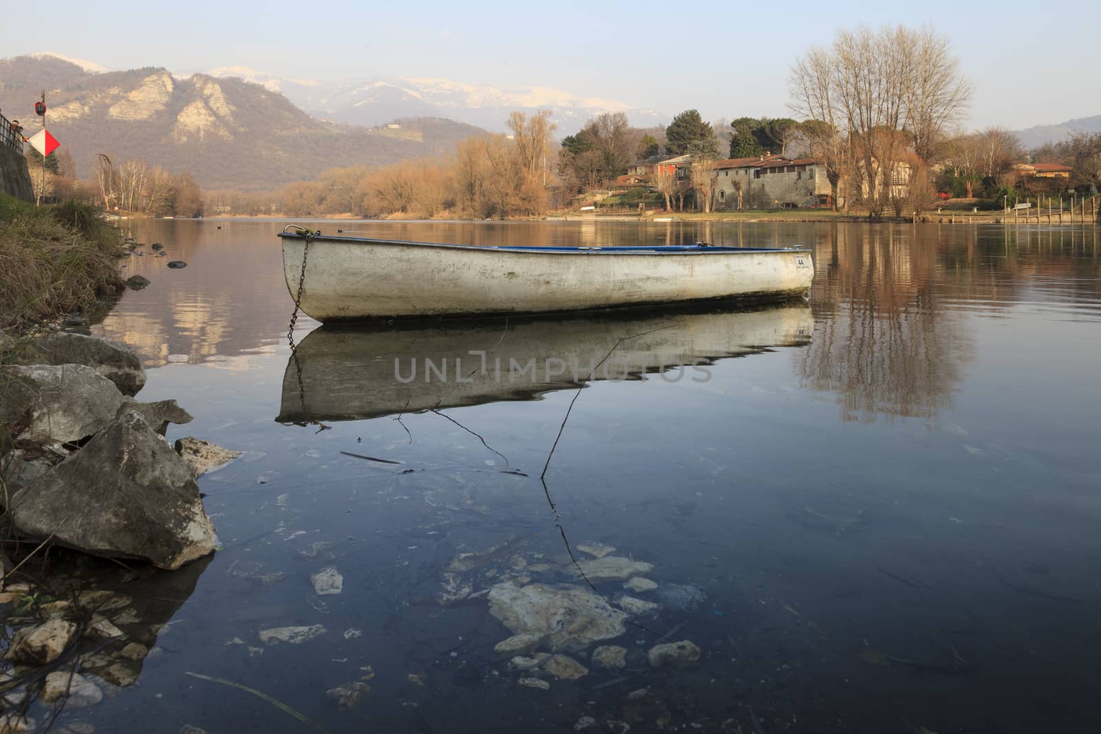 An old boat reflected on the rived with the mountains in the background. Brivio d’Adda, Milan, Italy