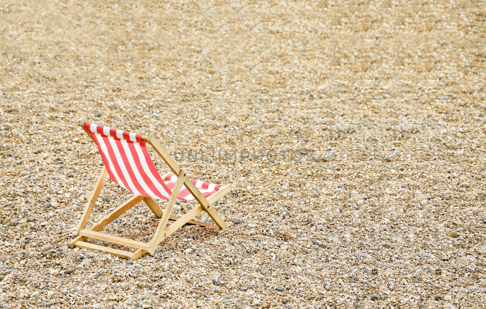 single wooden deck chair on a deserted pebbled beach