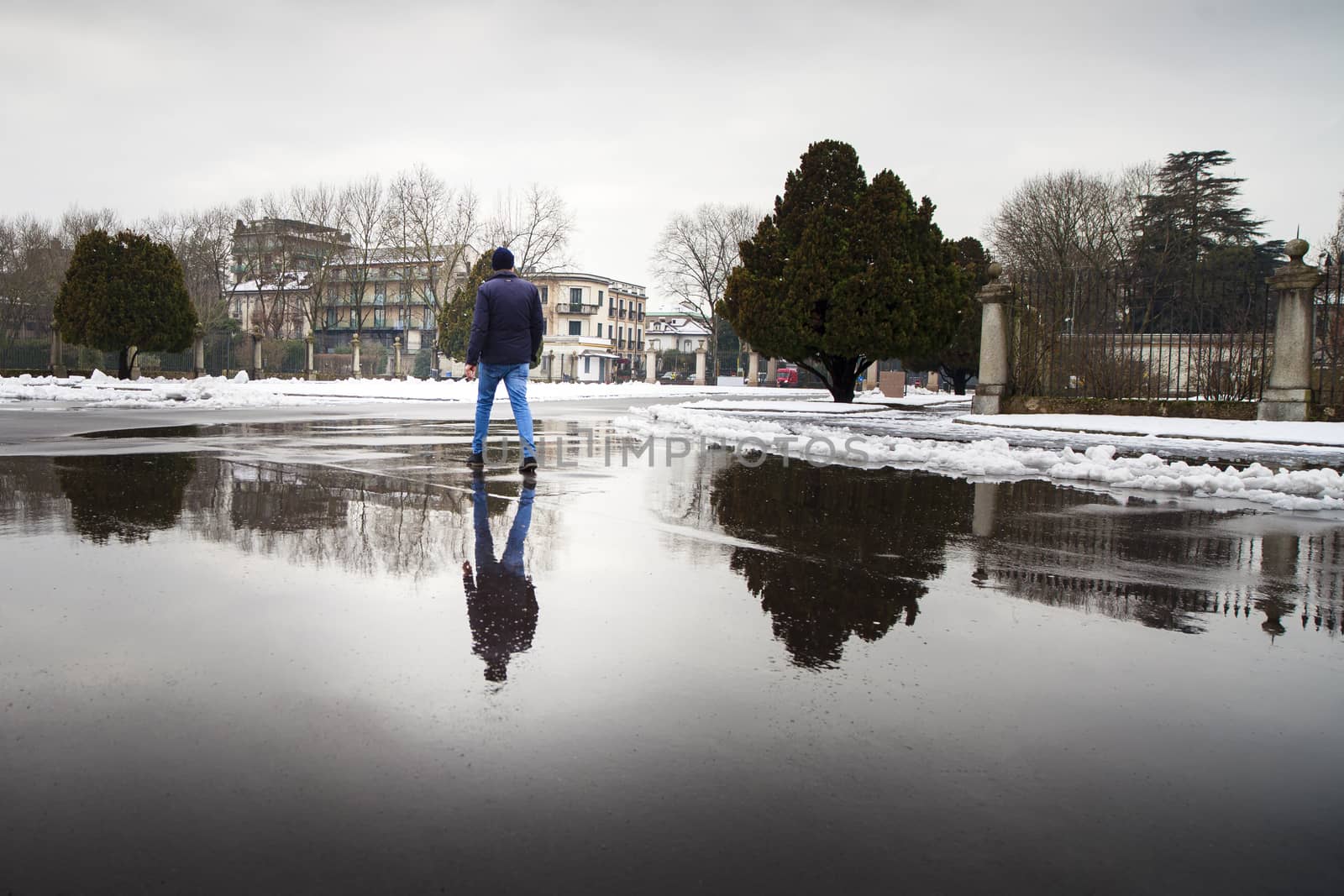 A young man and his reflection walking on a pluddle during a winter cold day