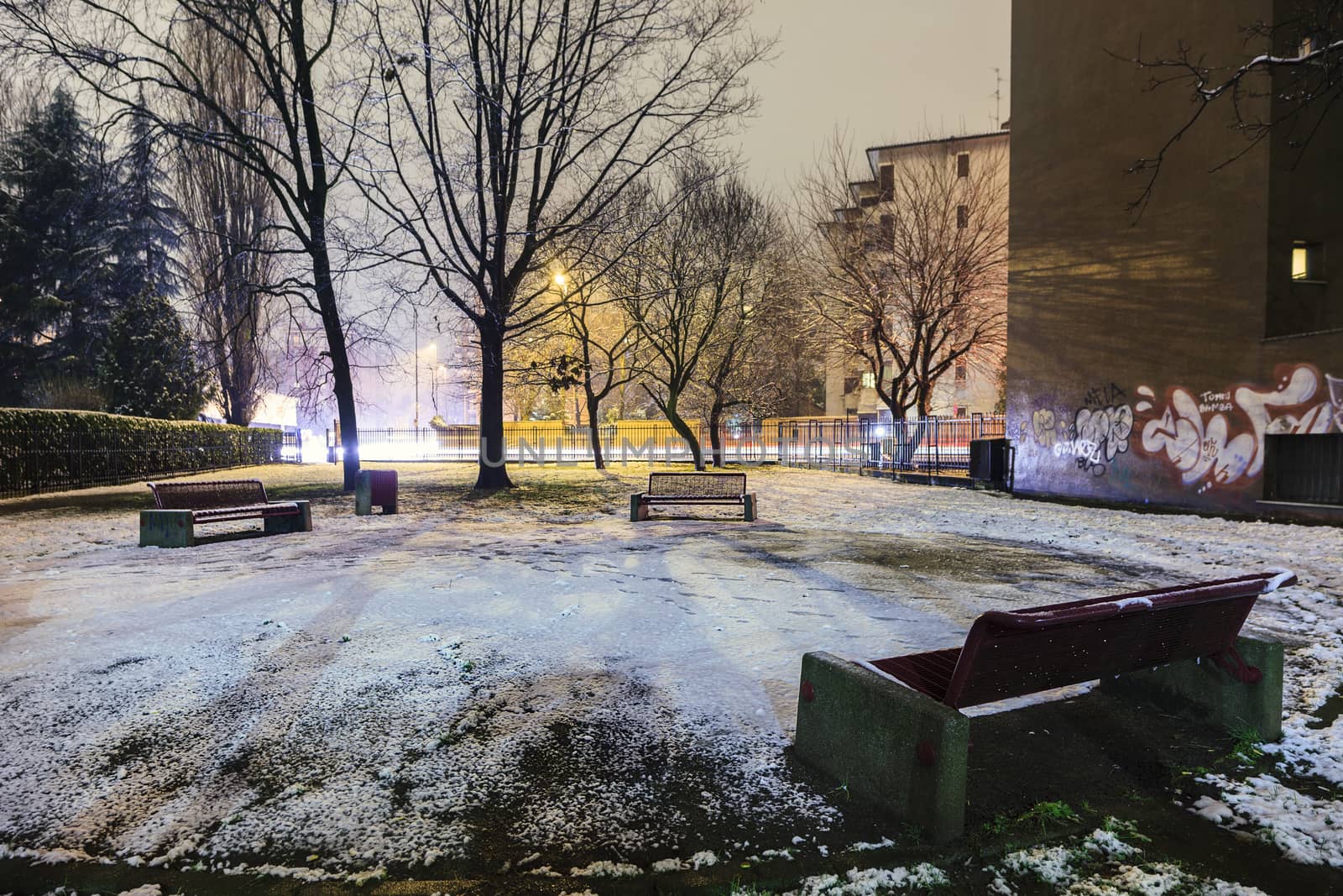 A frozen solitary bench into a small city park covered by snow and ice, Monza, Italy 