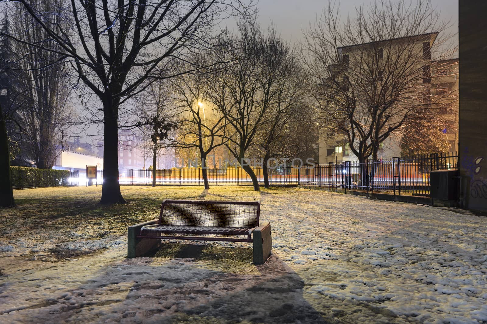 A frozen solitary bench into a small city park covered by snow and ice, Monza, Italy