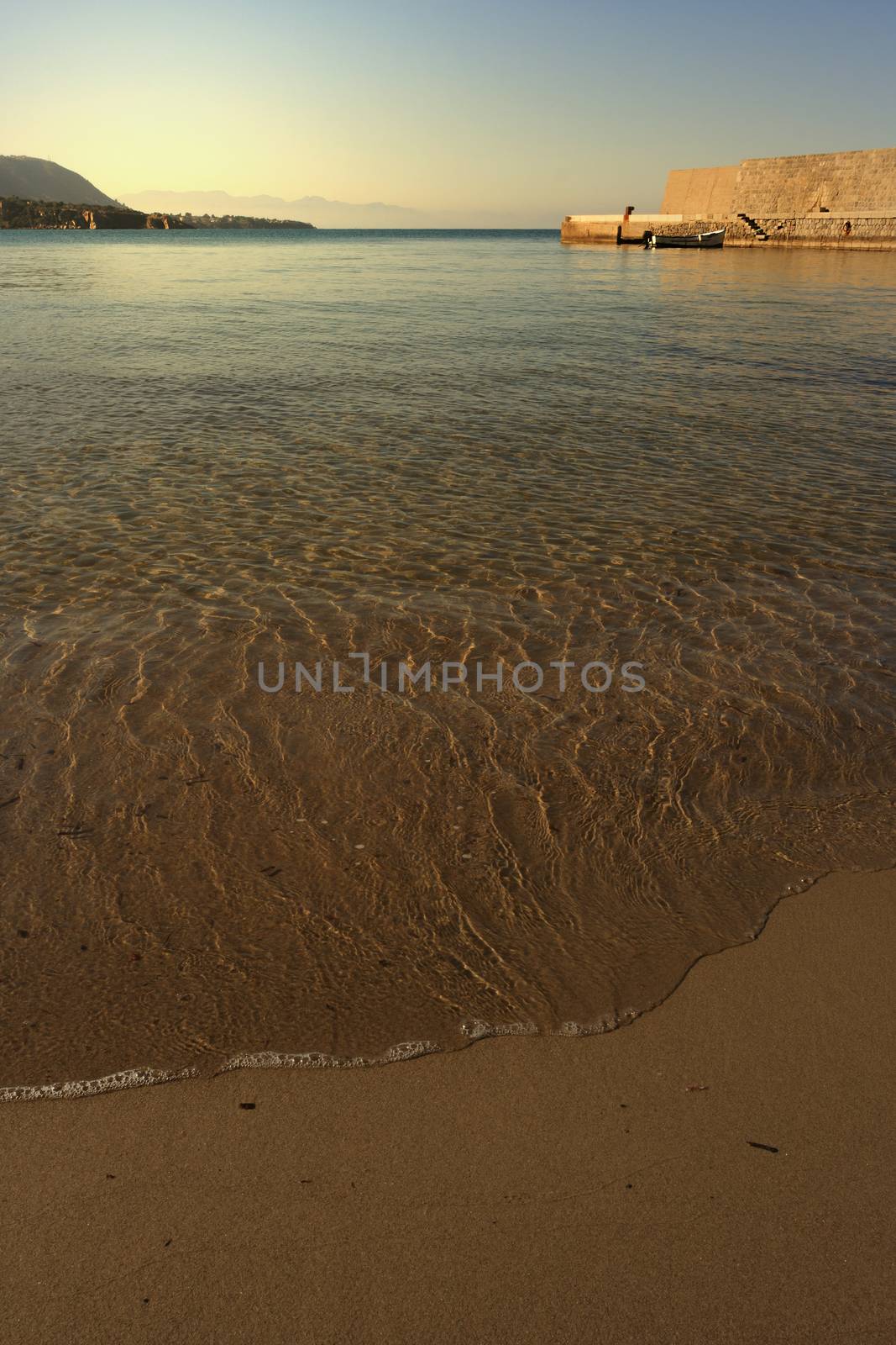 A piece of sandy bay illuminated by the sun with a boat in the background, Cefalu, Italy 
