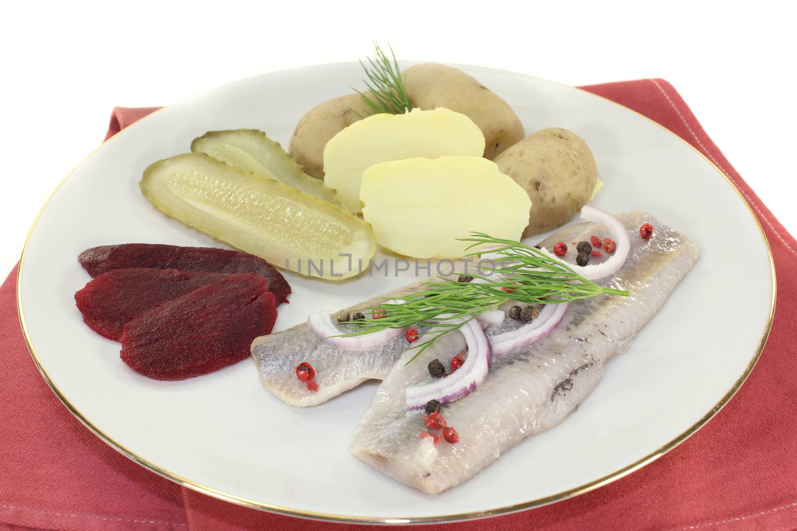 a plate of pickled herring fillet, boiled potatoes, beetroot and pickled gherkins