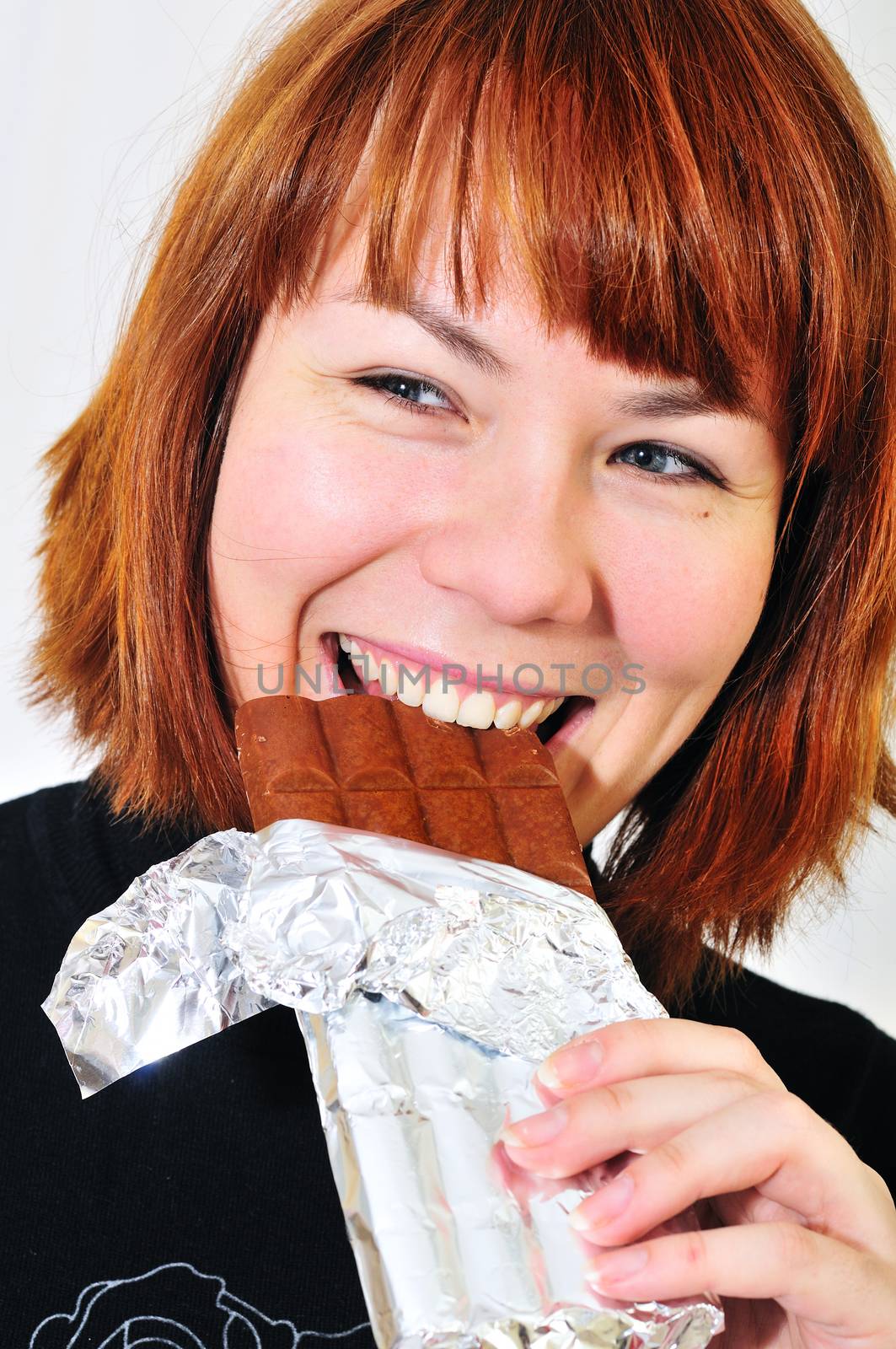 Young redheaded woman eating a chocolate bar 