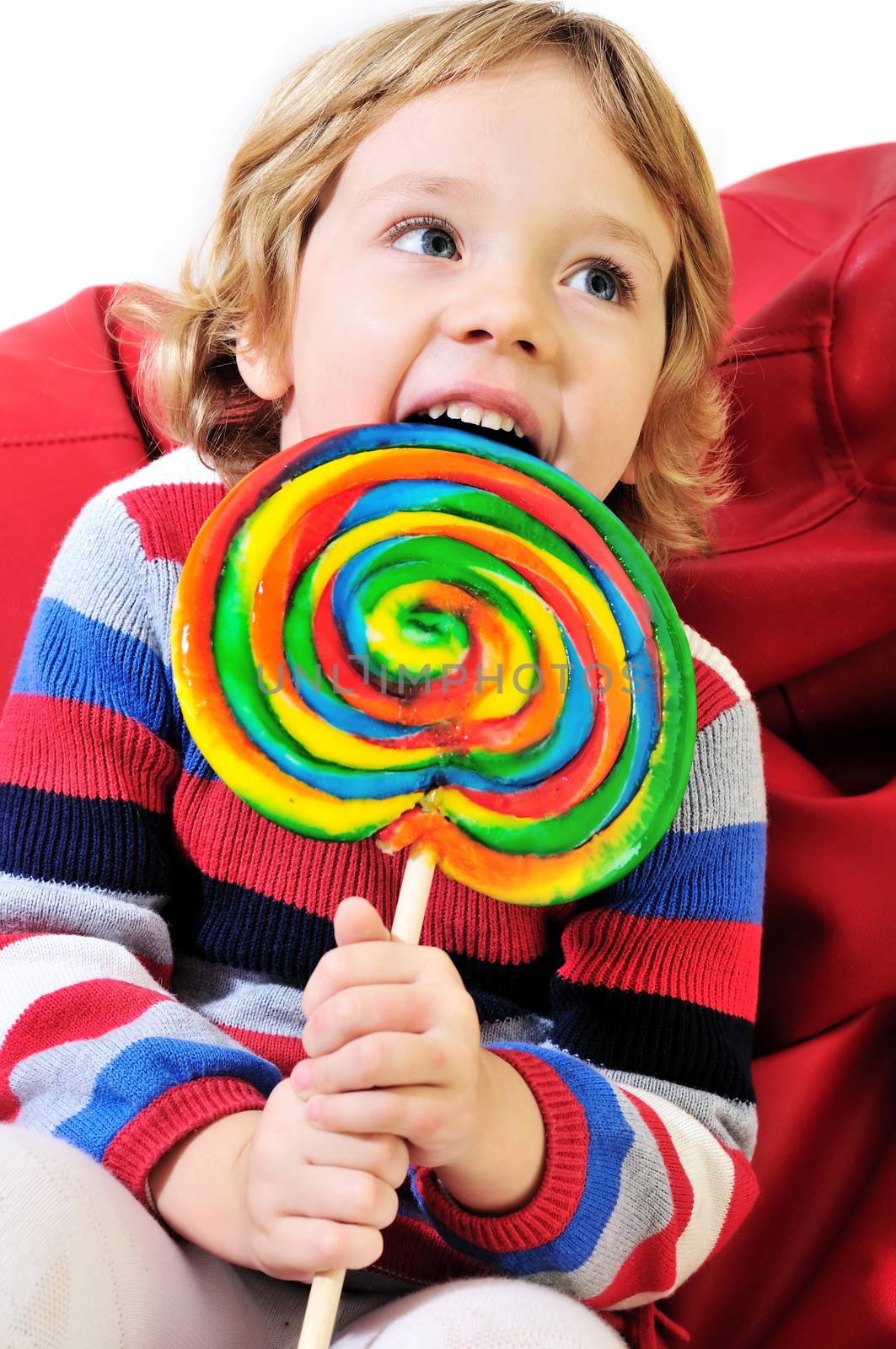 little girl eating big colorful lollipop  and sitting on the arm-chair