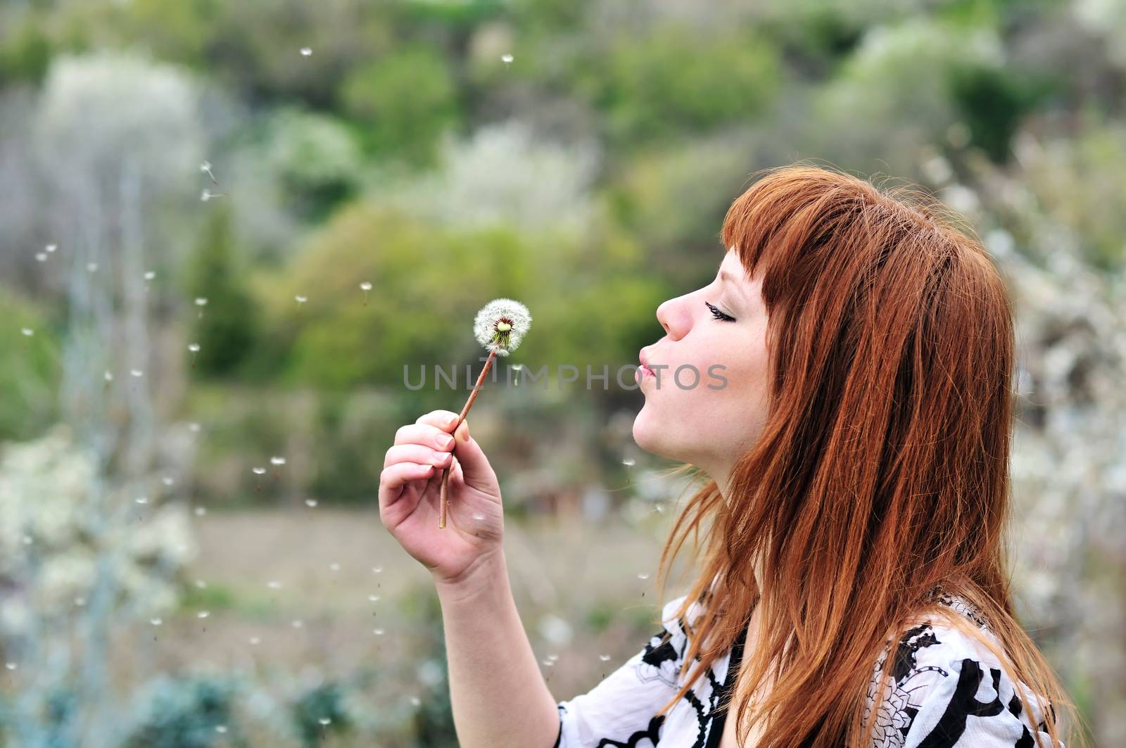pretty redheaded teen girl blowing on dandelion 