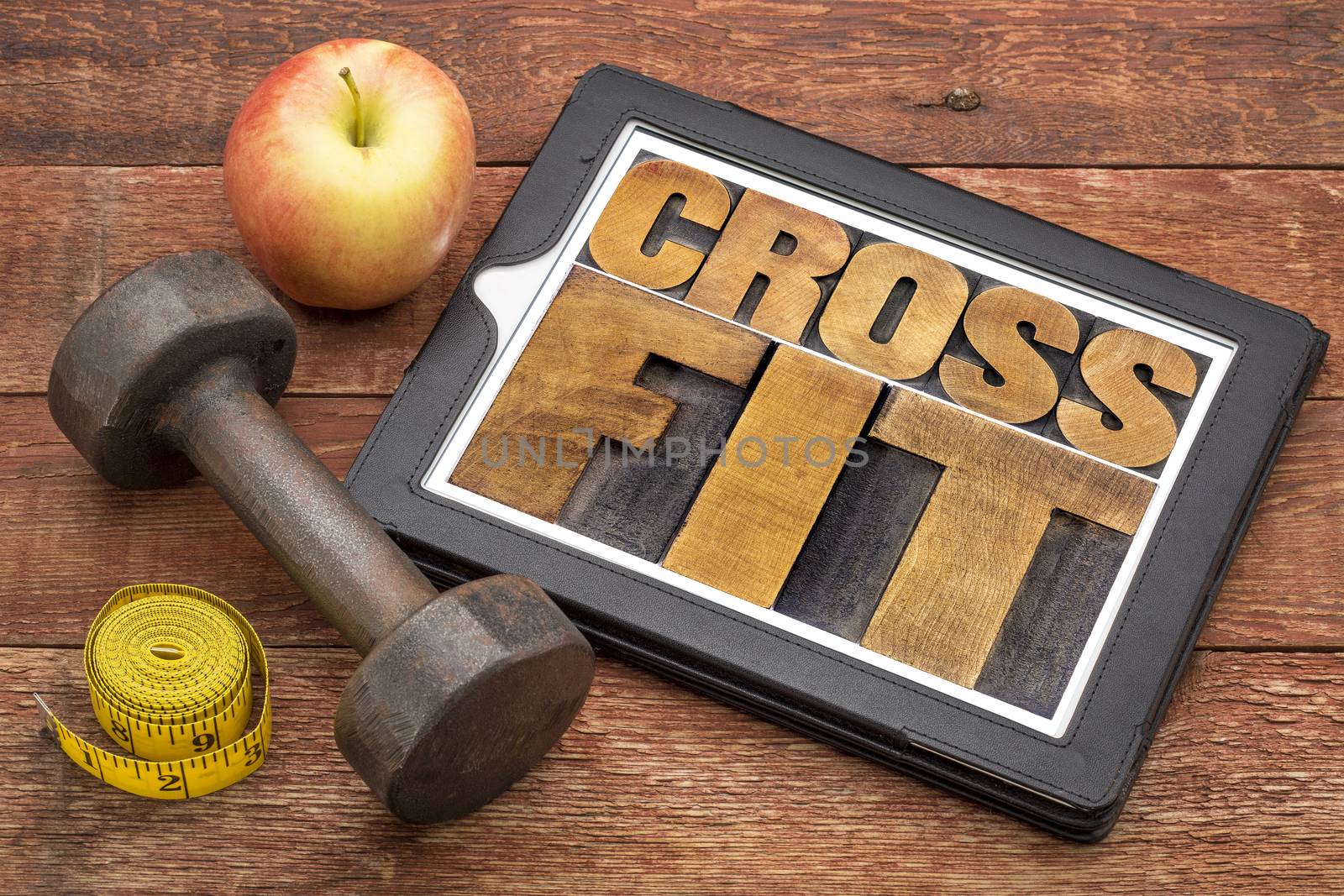 crossfit word abstract - text in letterpress wood type on a digital tablet with dumbbell and tape measure - fitness concept