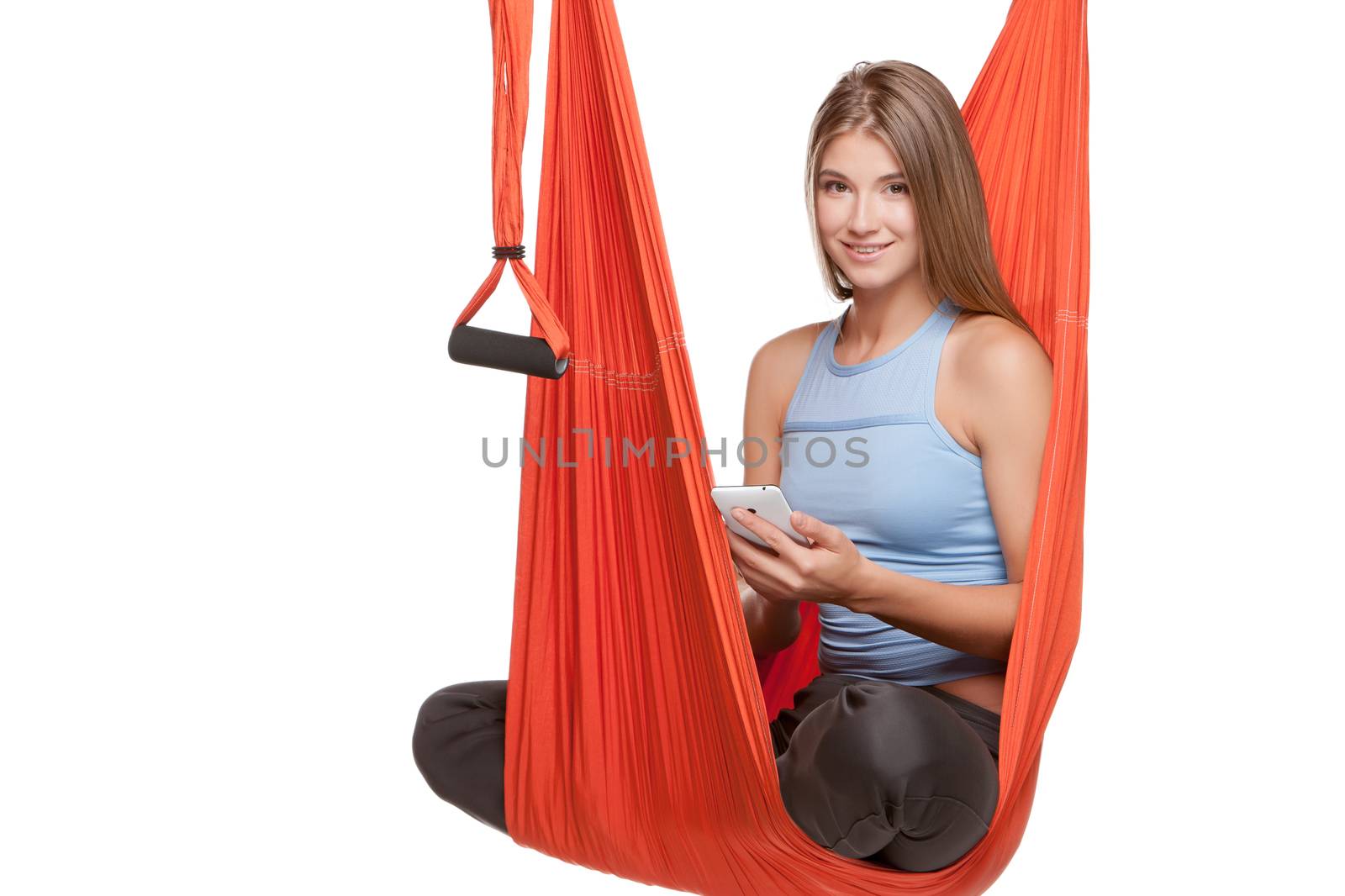 Young woman sitting in red hammock for anti-gravity aerial yoga with phone on a white background.