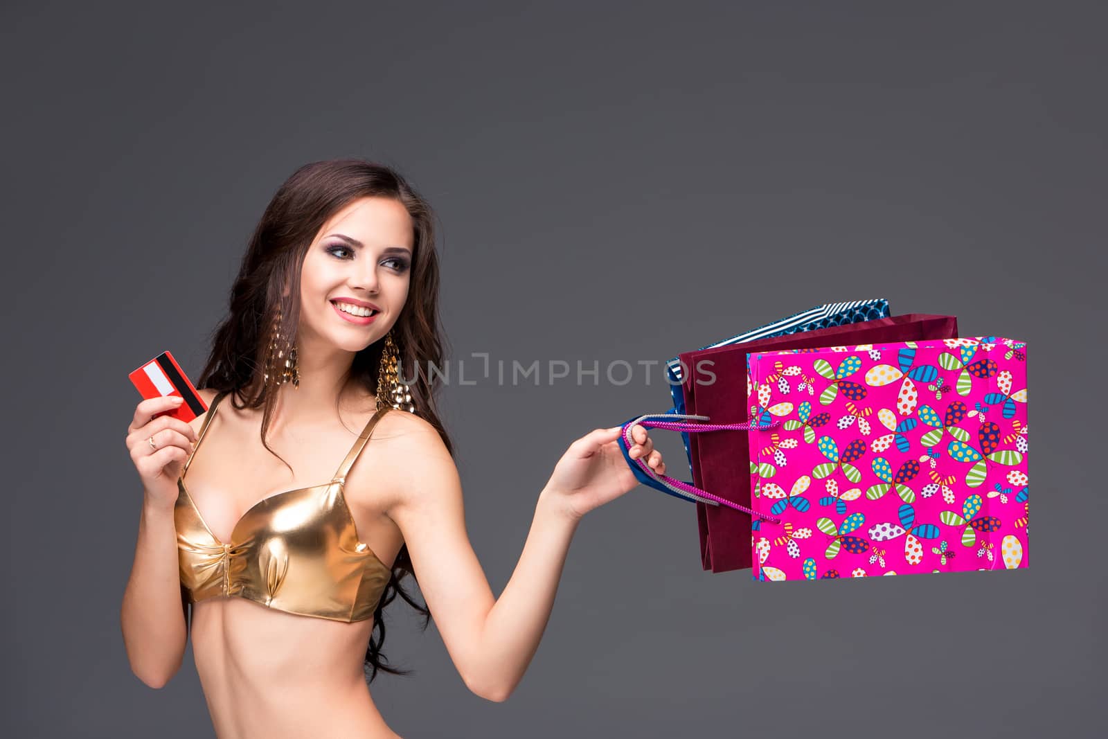 Young woman in a gold swimsuit with shopping bags and credit card on a gray background