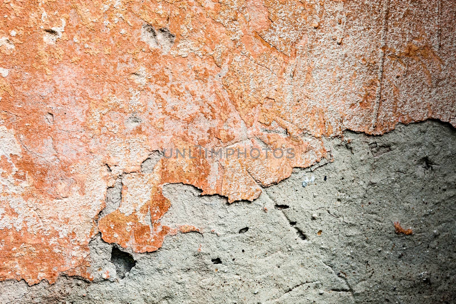 Concrete surface with the remains of orange paint and whitewash and partly fallen plaster.