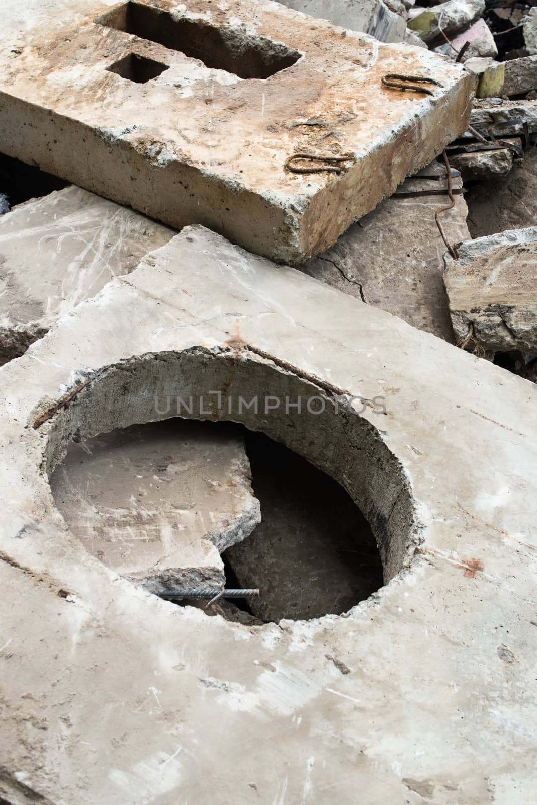 Concrete block with the manhole opening on the pile of damaged concrete blocks. 