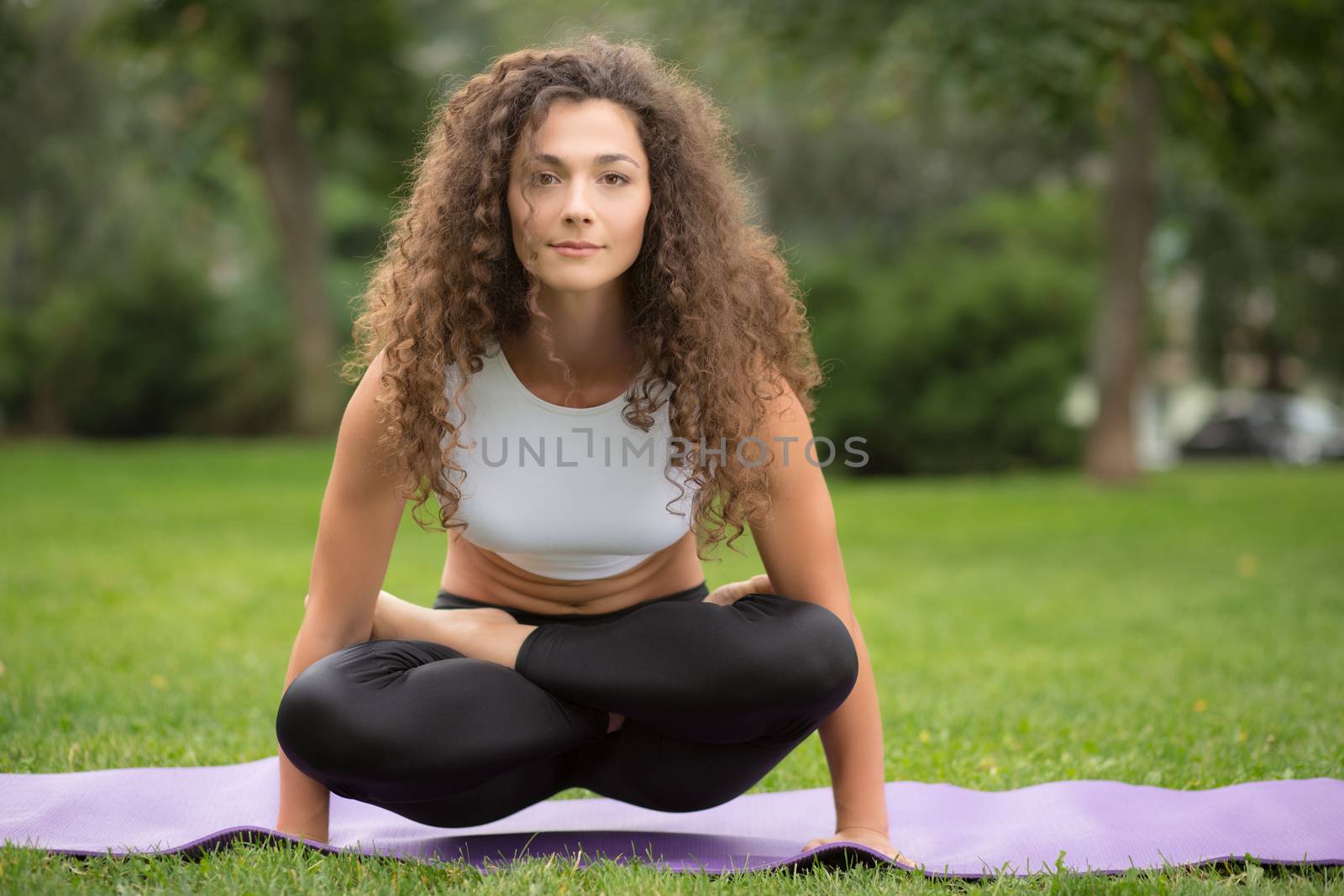 Pretty woman doing yoga exercises in outdoor park setting, nice green grass background 