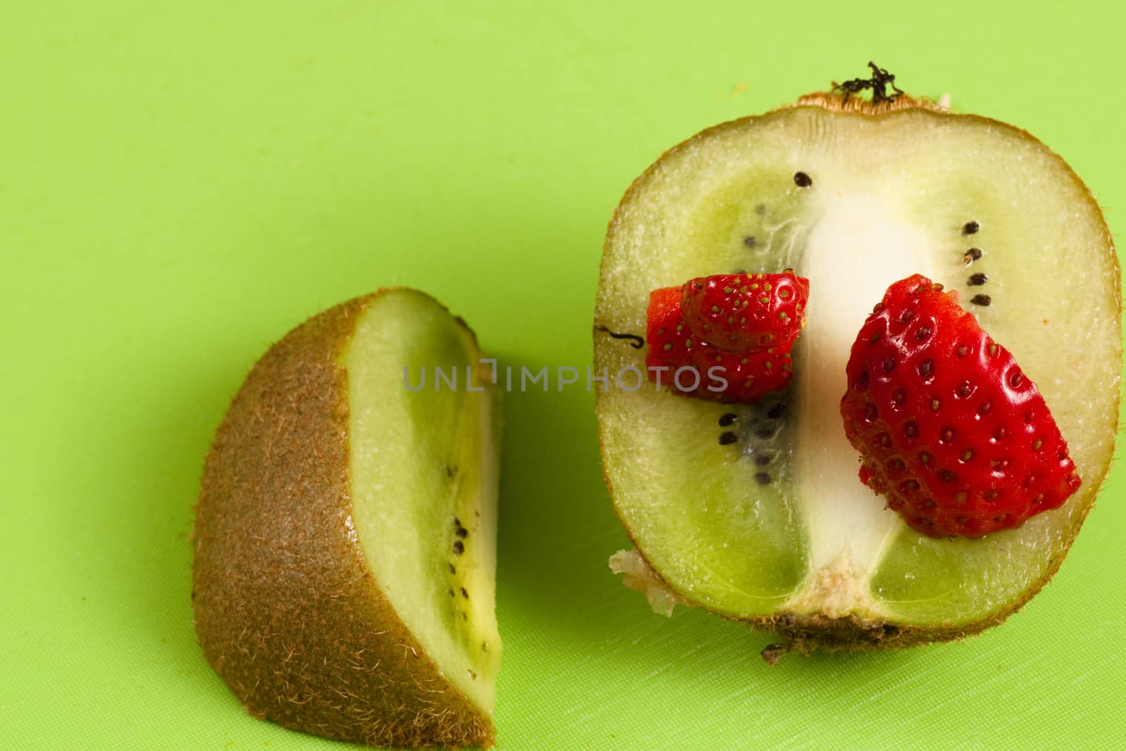 kiwi in half with over strawberries served on a green floor