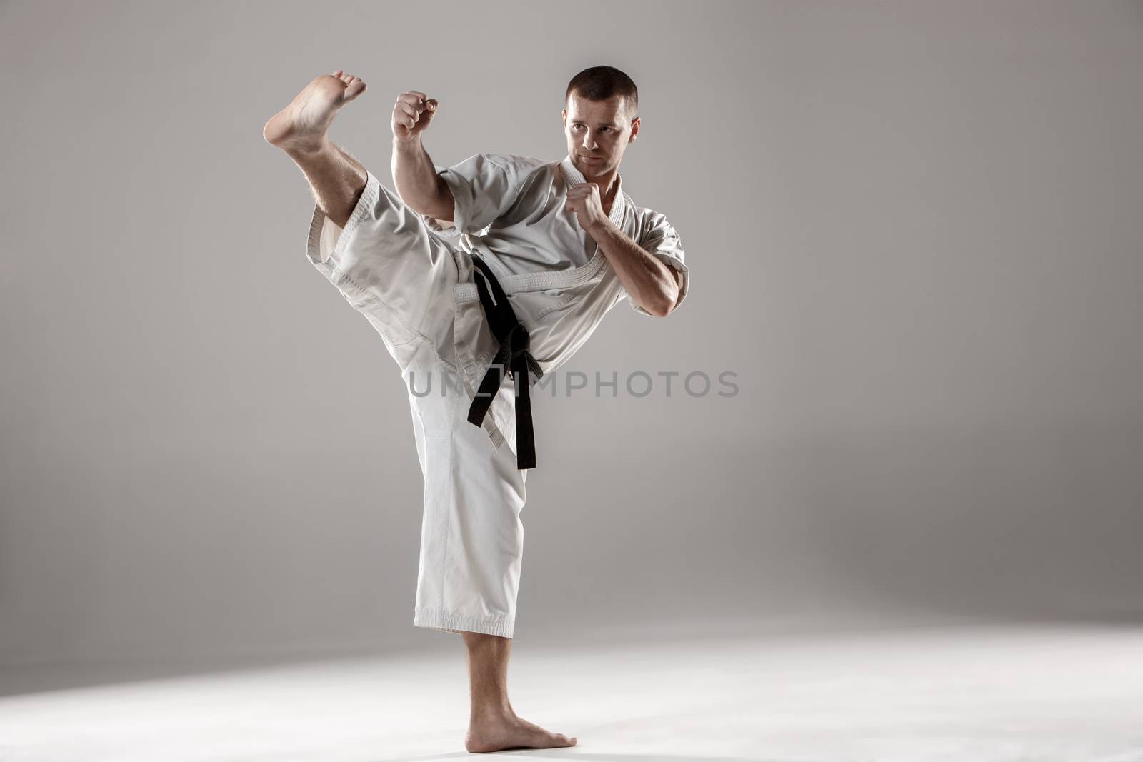 Man in white kimono and black belt training karate over gray background.