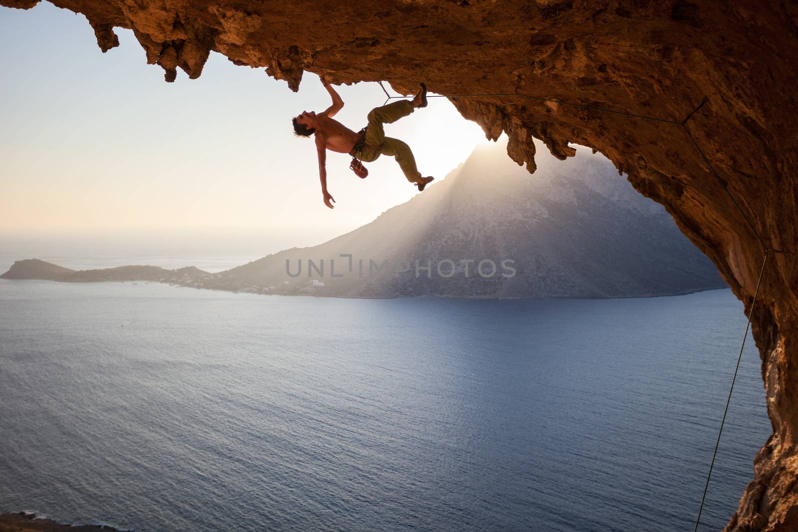 Rock climber climbing along roof in cave at sunset by photobac
