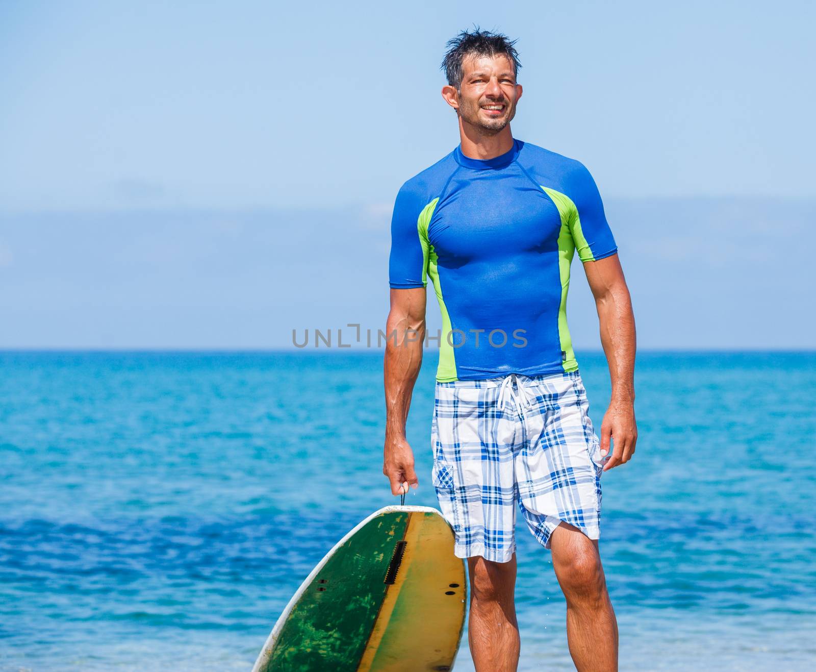 Strong young surf man at the beach with a surfboard.