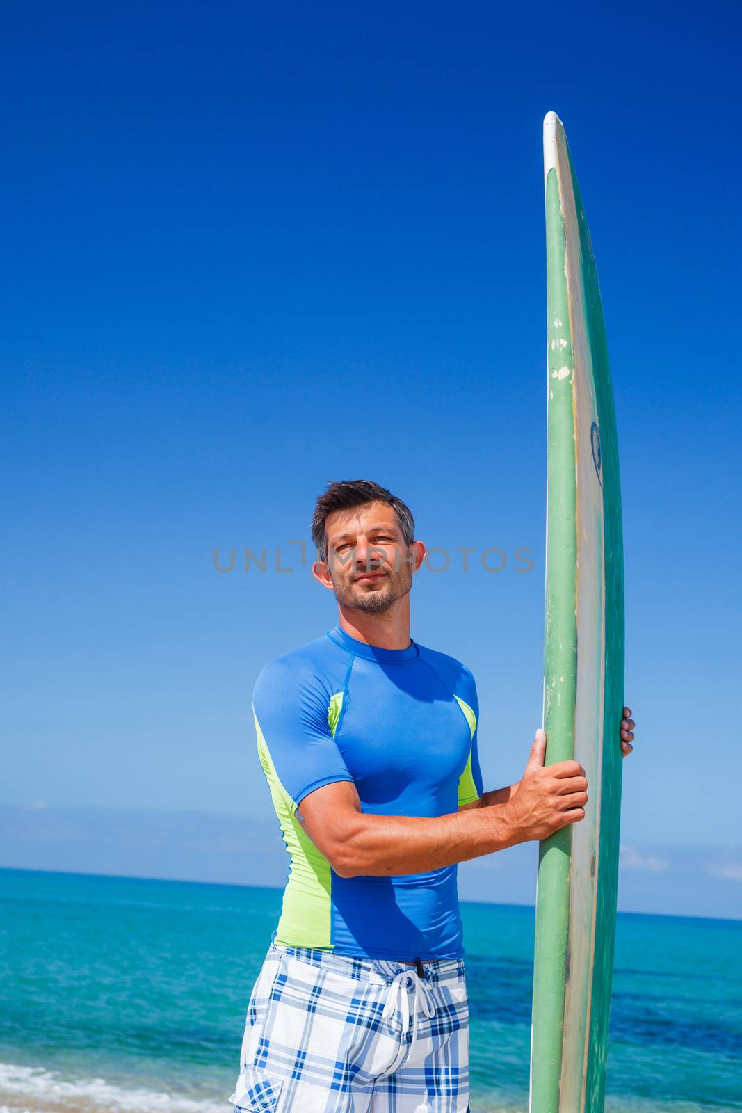 Portrait of strong young surf man at the beach with a surfboard.