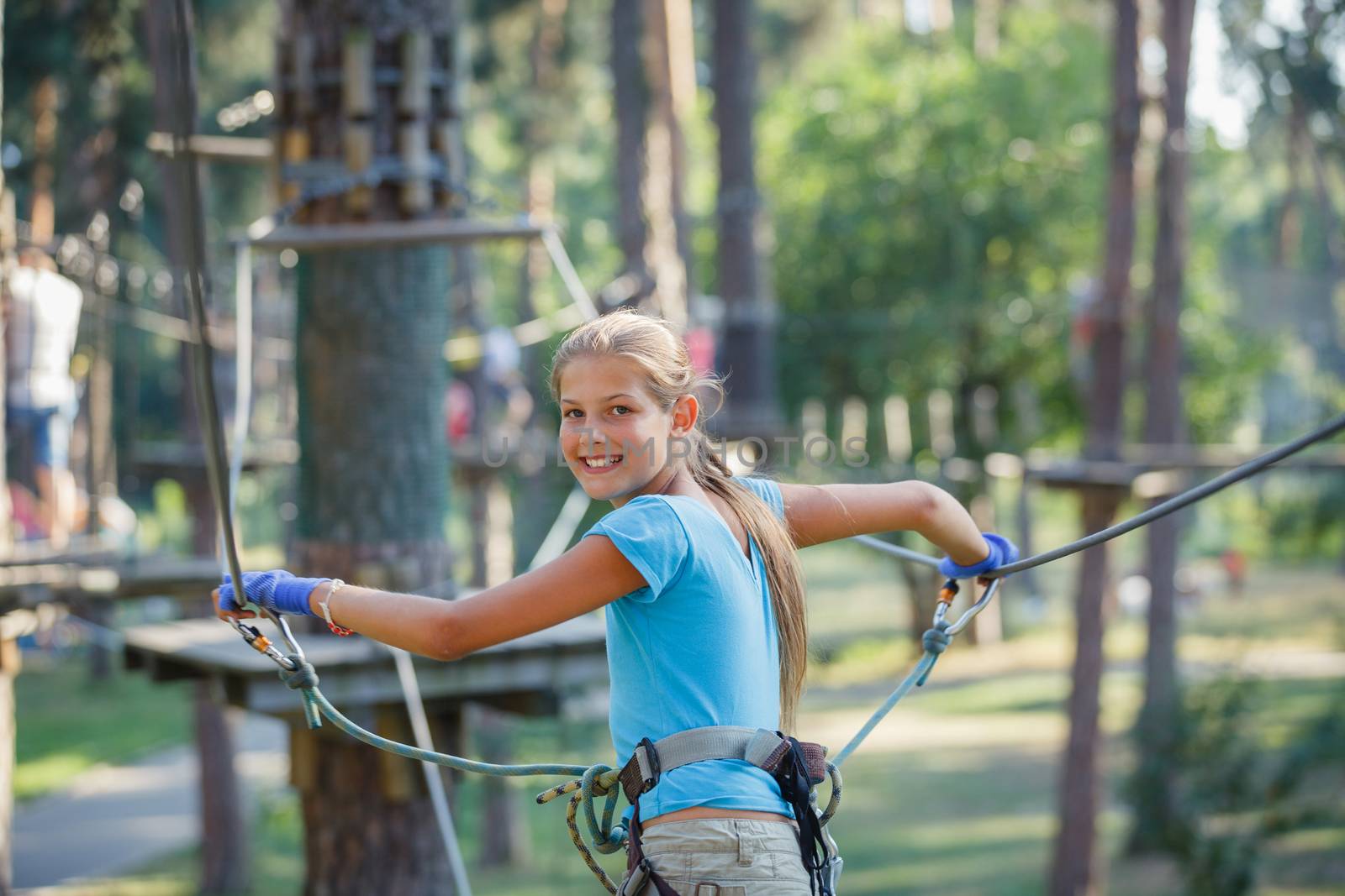 Portrait of happy school girl enjoying activity in a climbing adventure park on a summer day