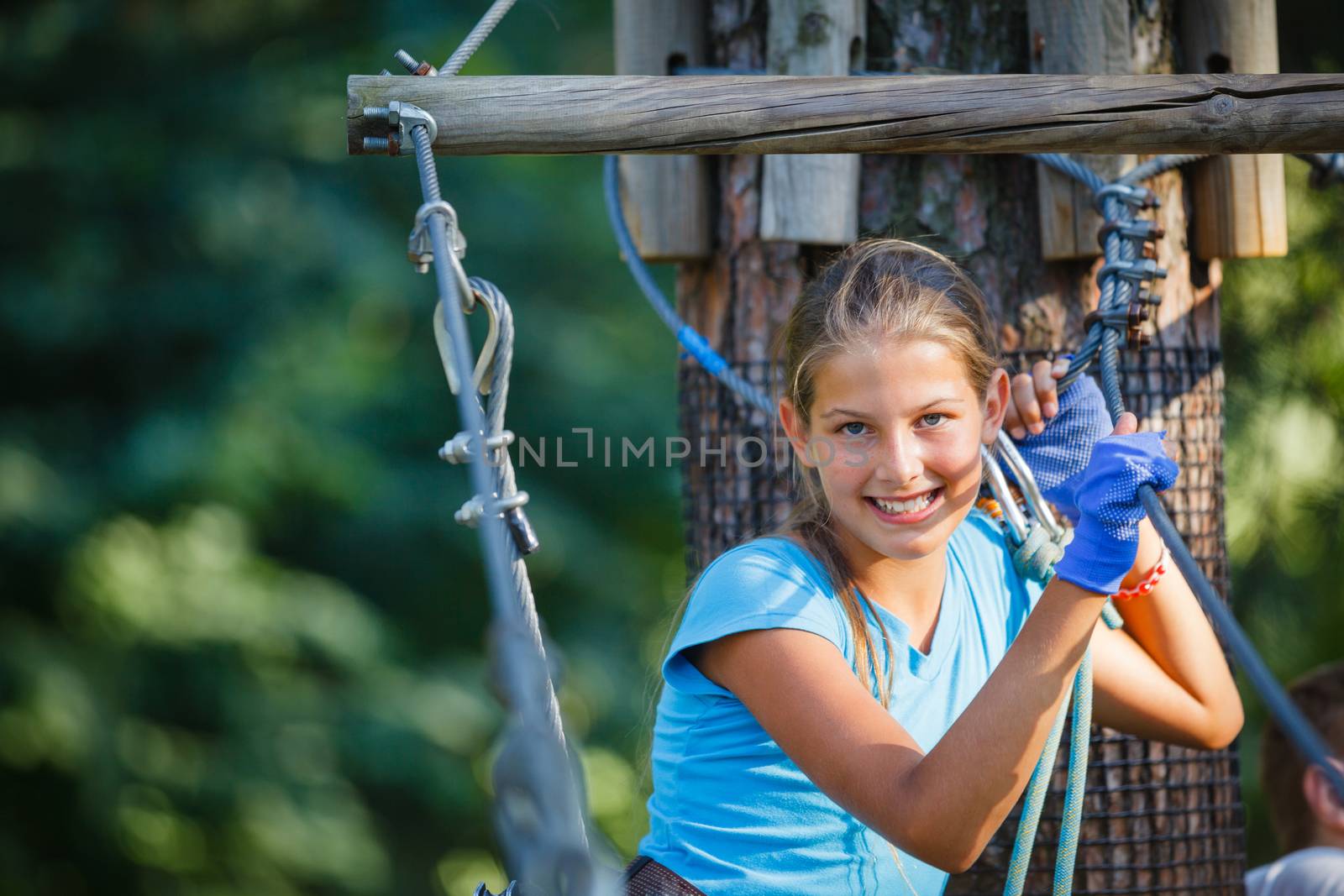 Portrait of happy school girl enjoying activity in a climbing adventure park on a summer day