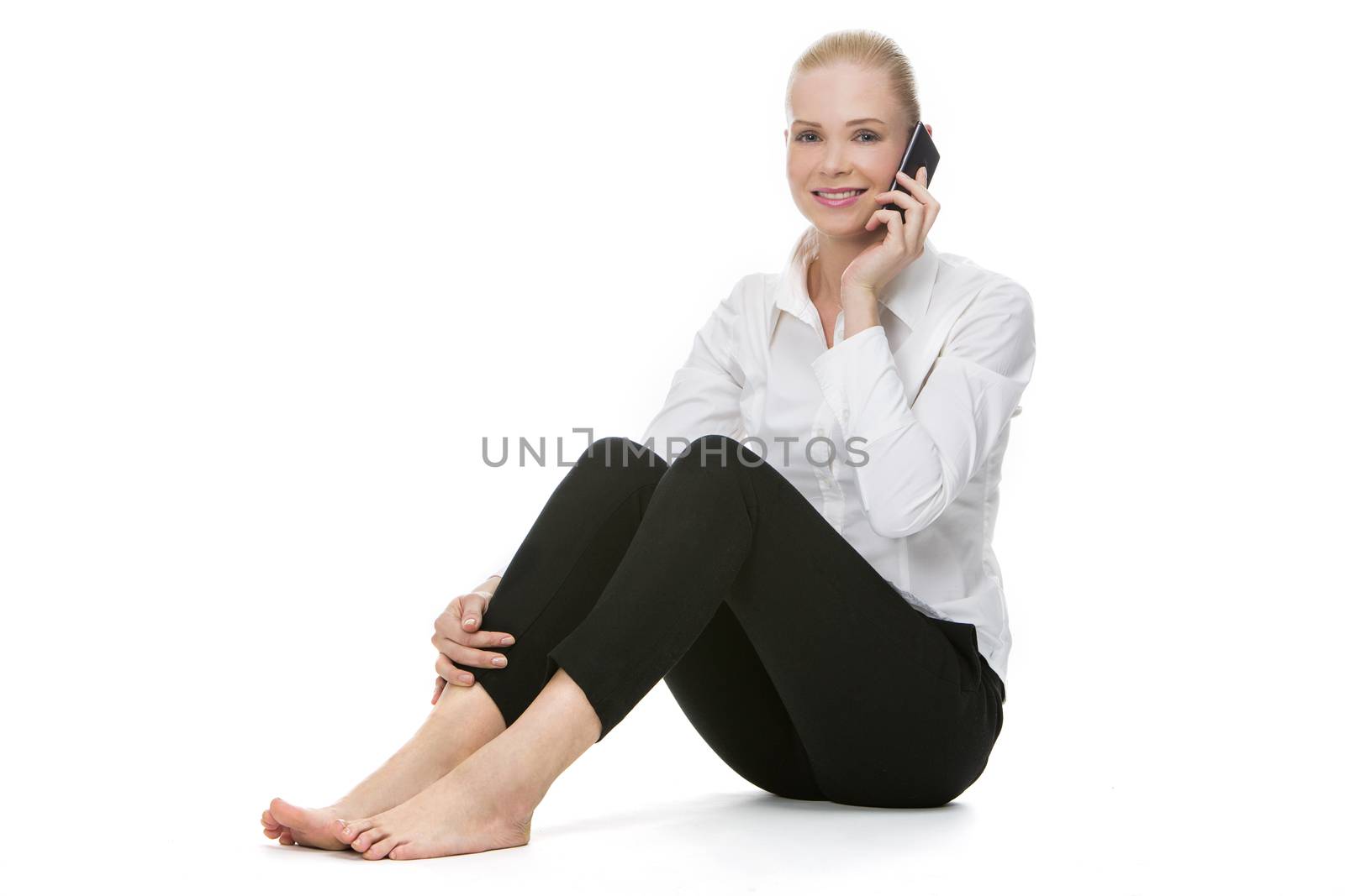 blonde smiling businesswoman seated on the floor and using mobile phone