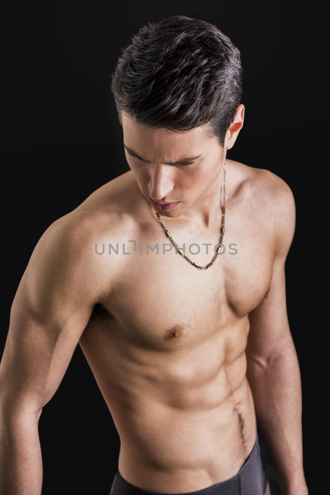 Handsome, fit young man wearing only underwear standing on black background, looking down