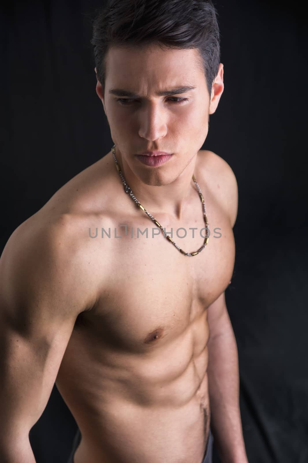 Handsome, fit young man wearing only underwear standing on black background, looking away
