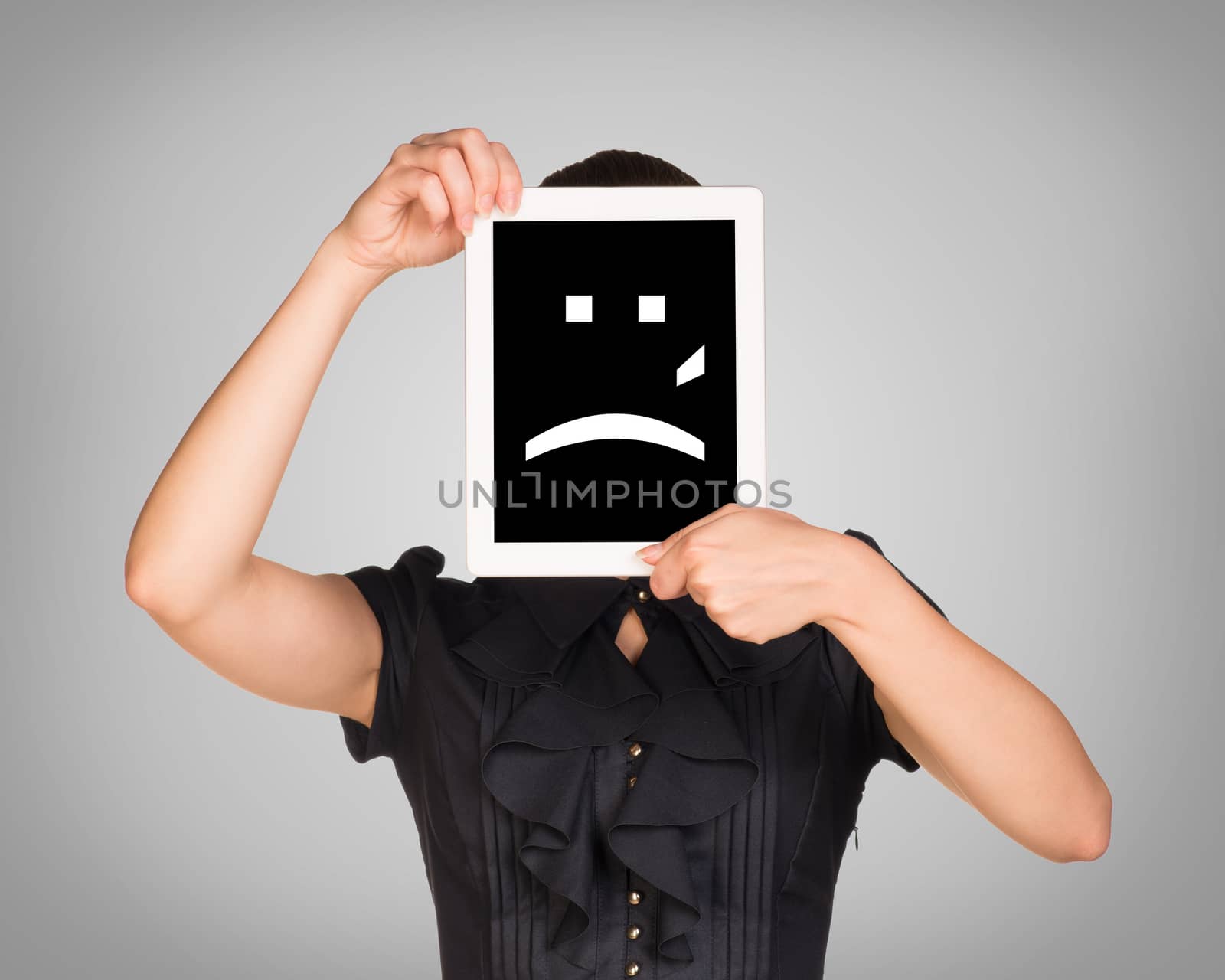 Girl in dress covered her face with tablet. On screen sad smiley. Gray background