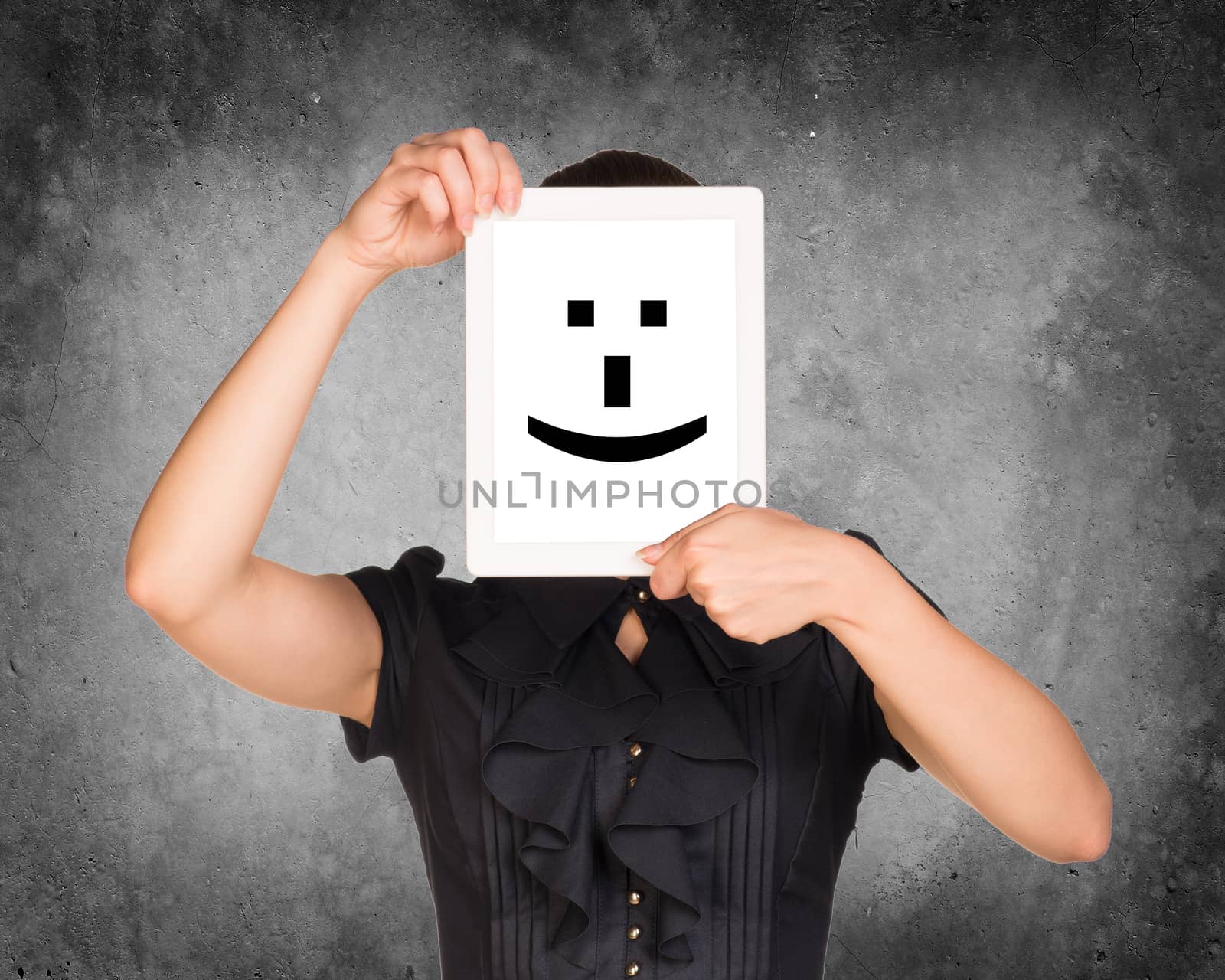 Girl in dress covered her face with tablet. On screen cheerful smiley. Concrete background