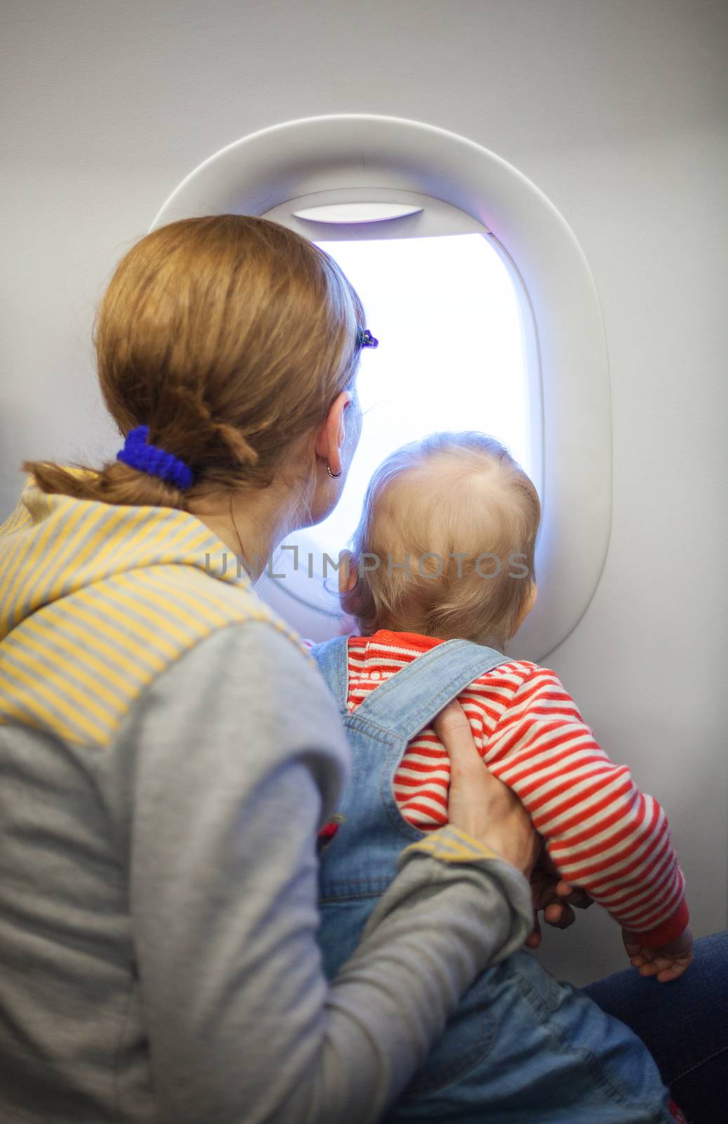 Mother and baby son looking out of window while on board of airplane
