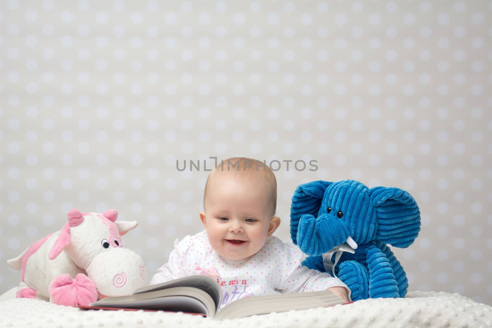 Smiling baby girl reading a book with little toy friends