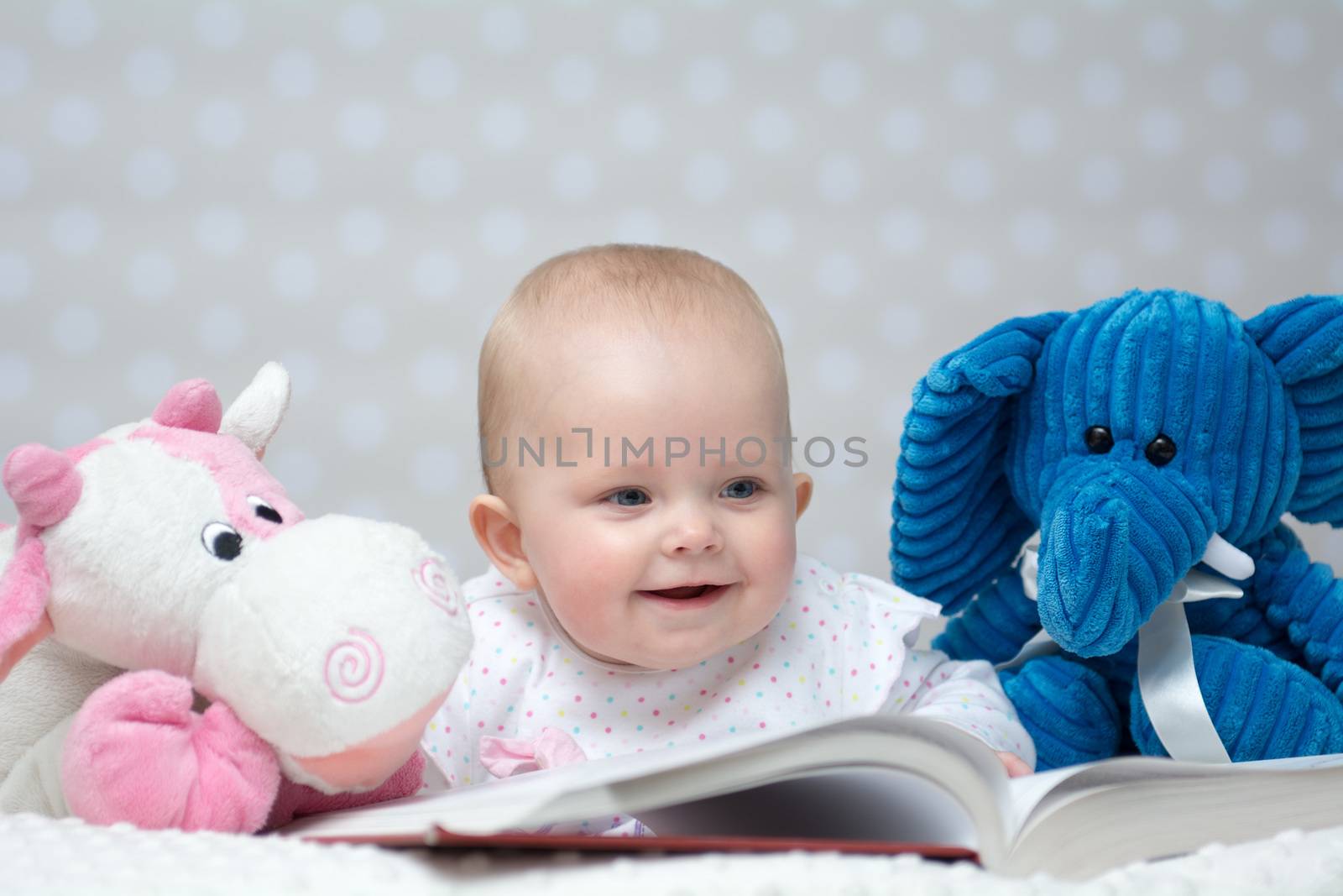 Happy baby girl reading a book with little toy friends