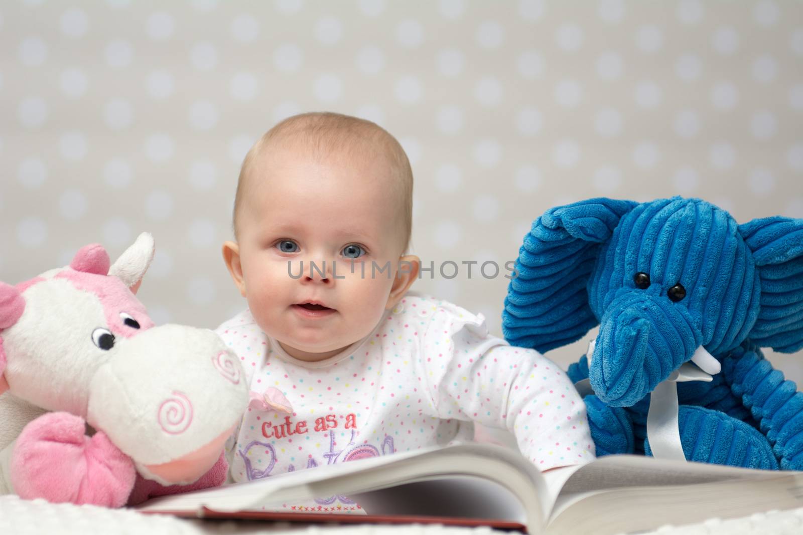 Baby girl reading a book with little toy friends and lookin at the camera