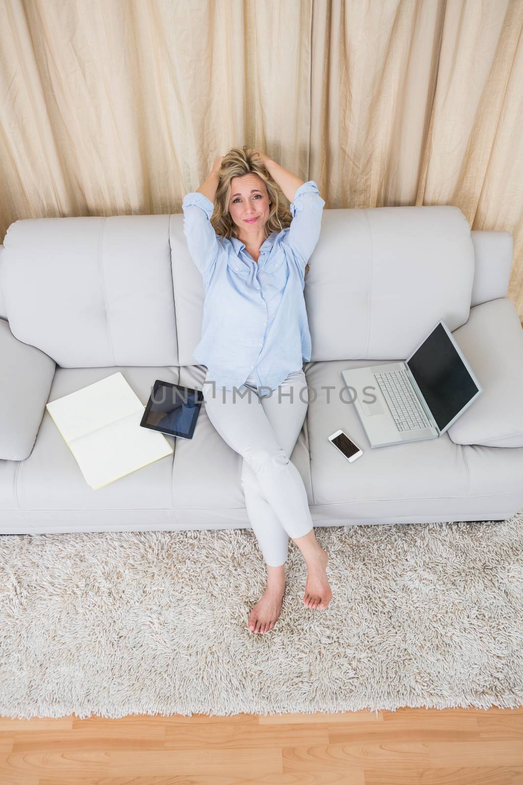 Pretty blonde sitting on couch near wirelesses technology at home in the living room