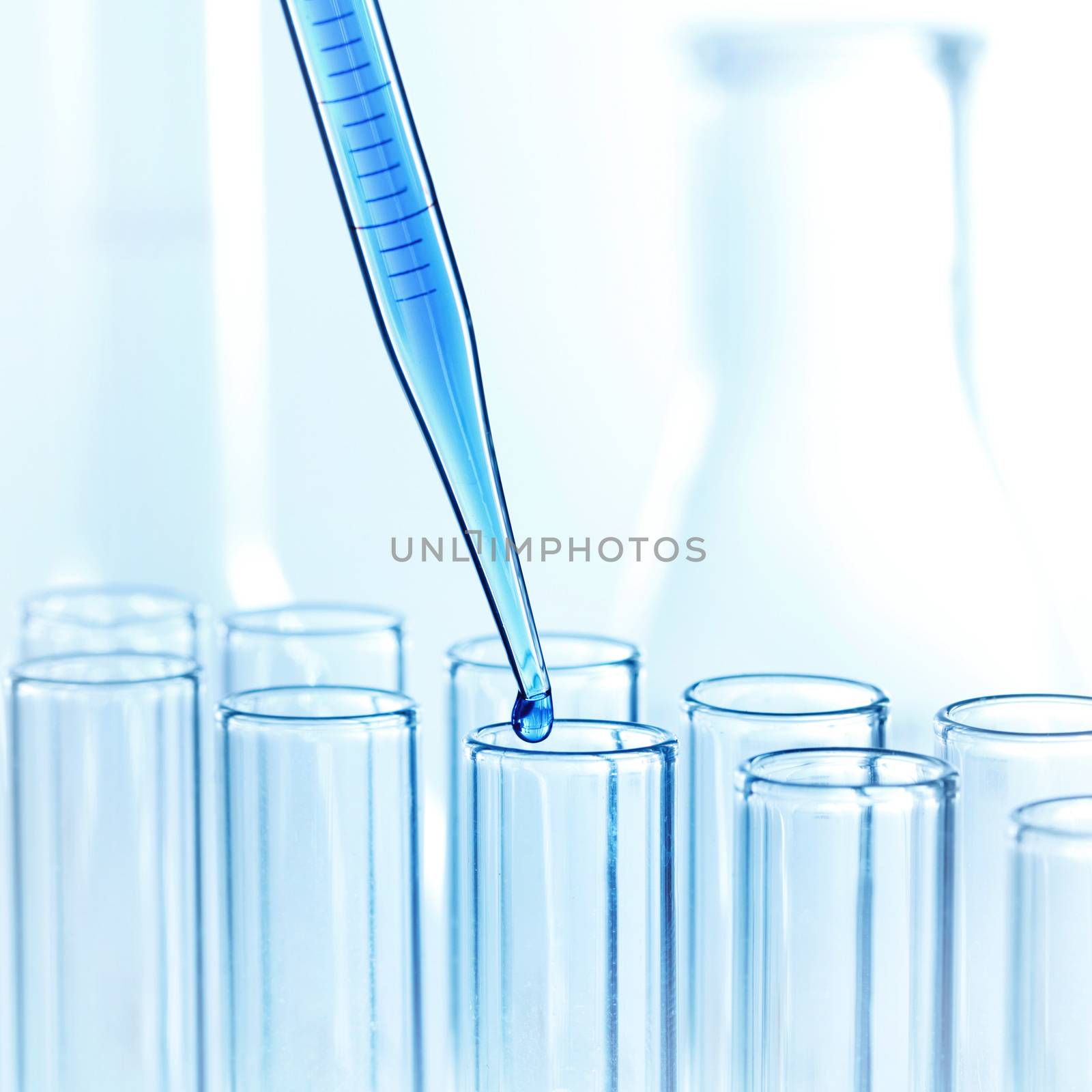 Laboratory pipette with drop of liquid over glass test tubes in a science research lab
