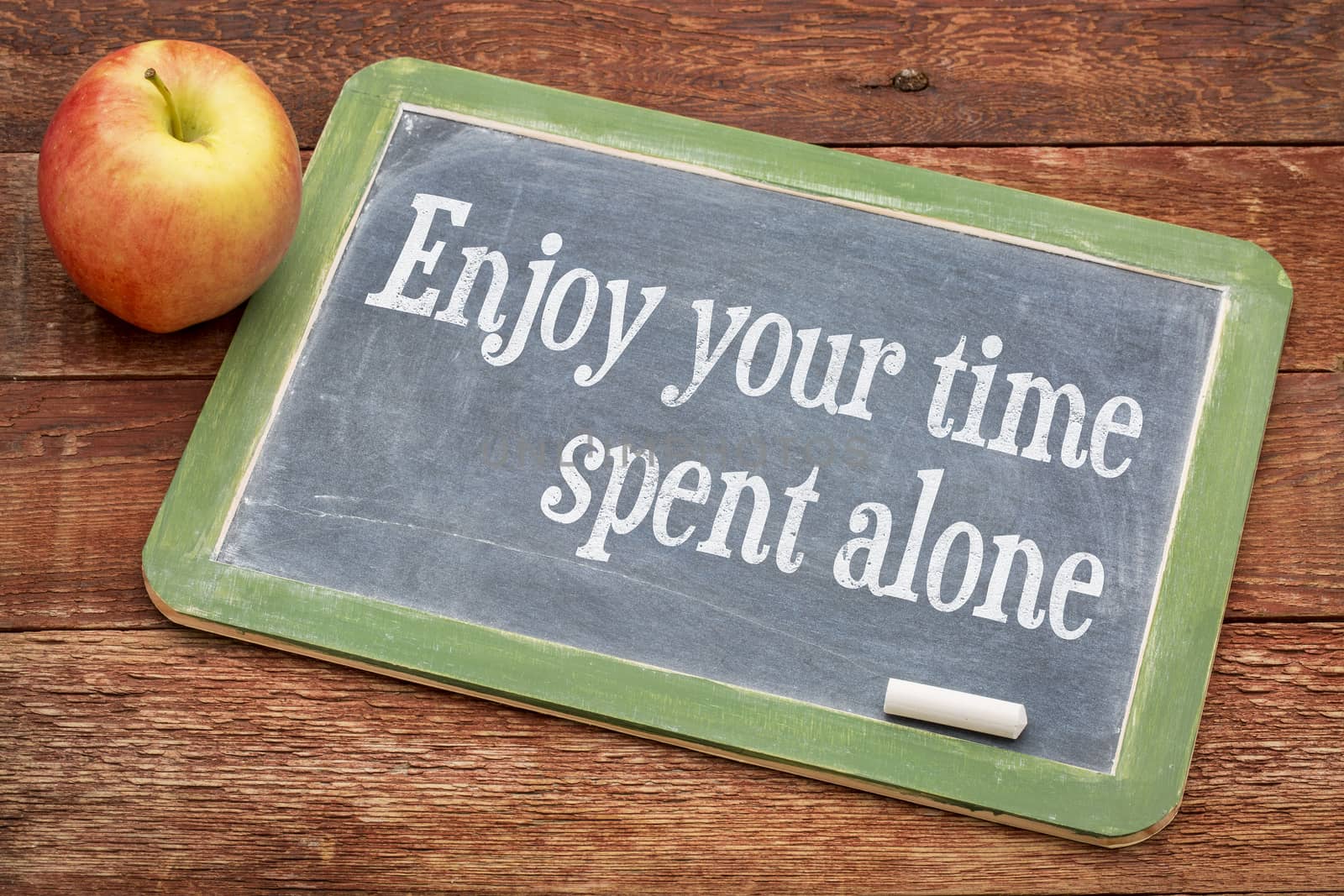 Enjoy your time spent alone - positive words on a slate blackboard against red barn wood