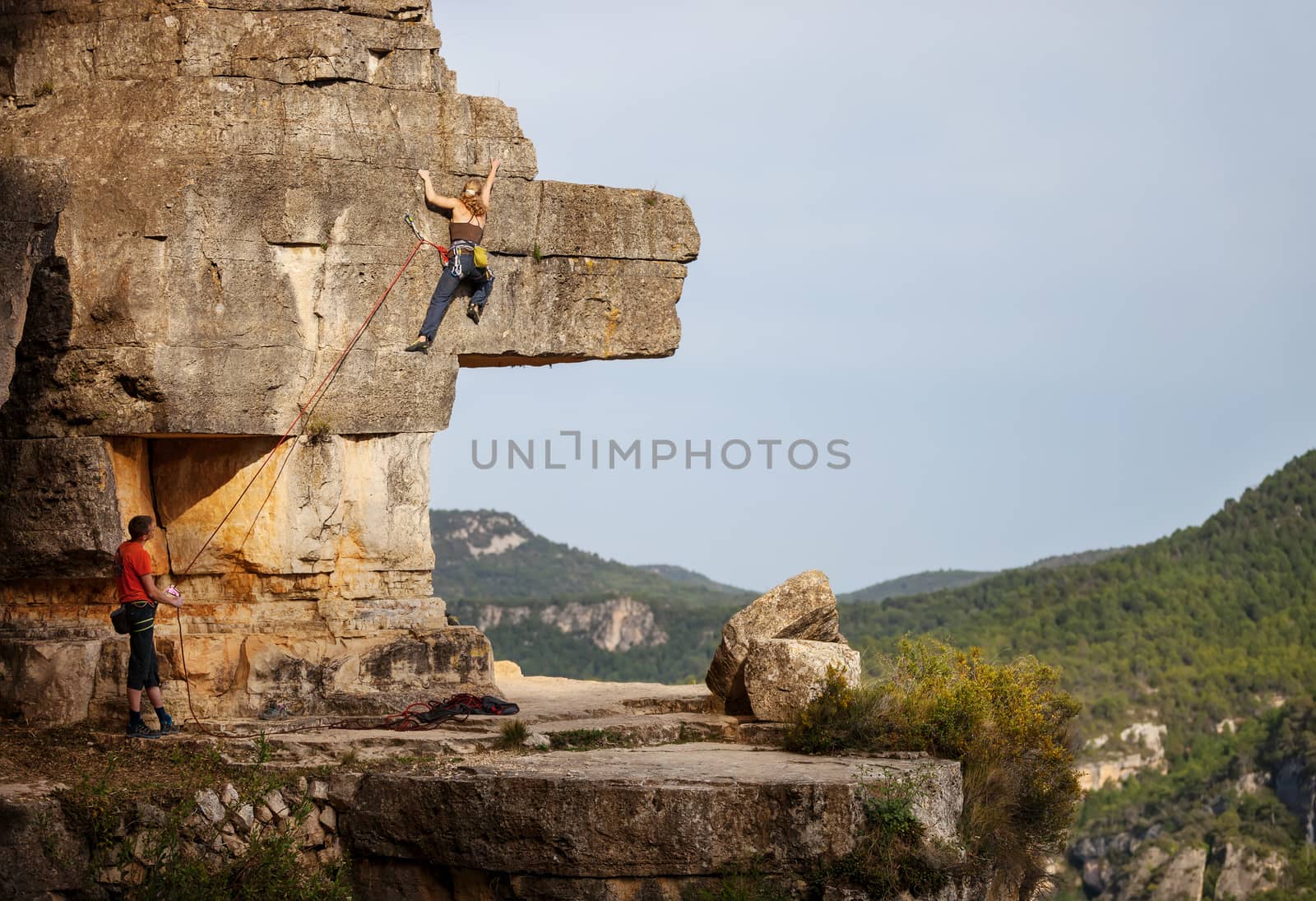 Woman climbing on cliff, male partner belaying by photobac