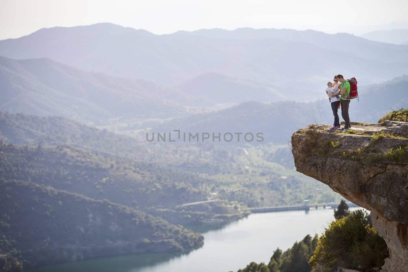 Happy young couple with little son standing on cliff over river