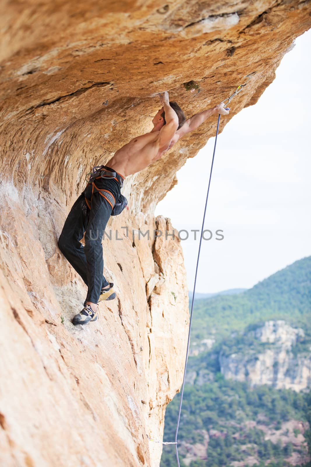Young man clipping rope while clinging to cliff by photobac