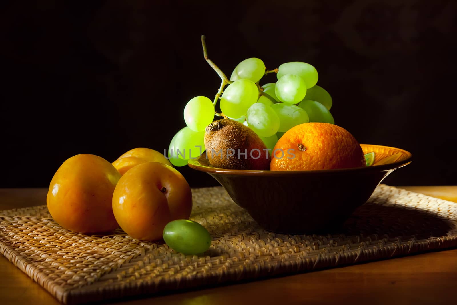 Still life. Yellow plums, grapes, oranges and kiwi on a wicker tray