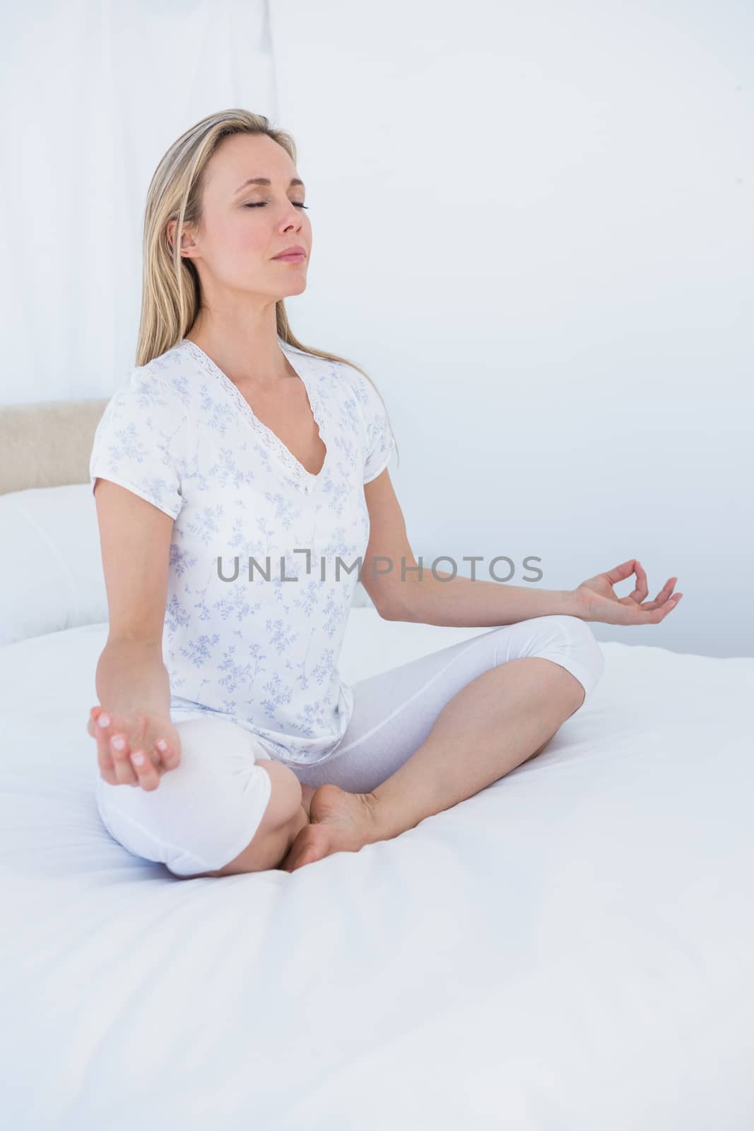 Blonde woman sitting in lotus pose in bed at home in the bedroom