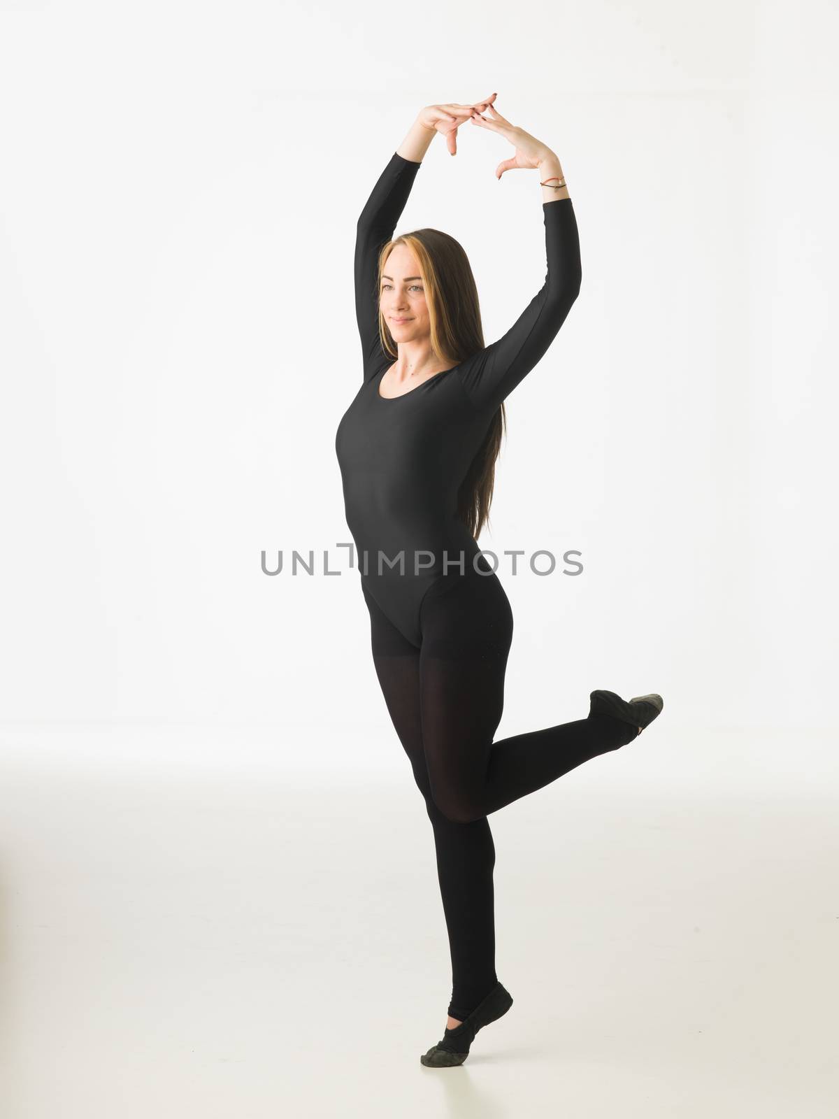 beautiful female ballet dancer standing on one leg, posing on white background