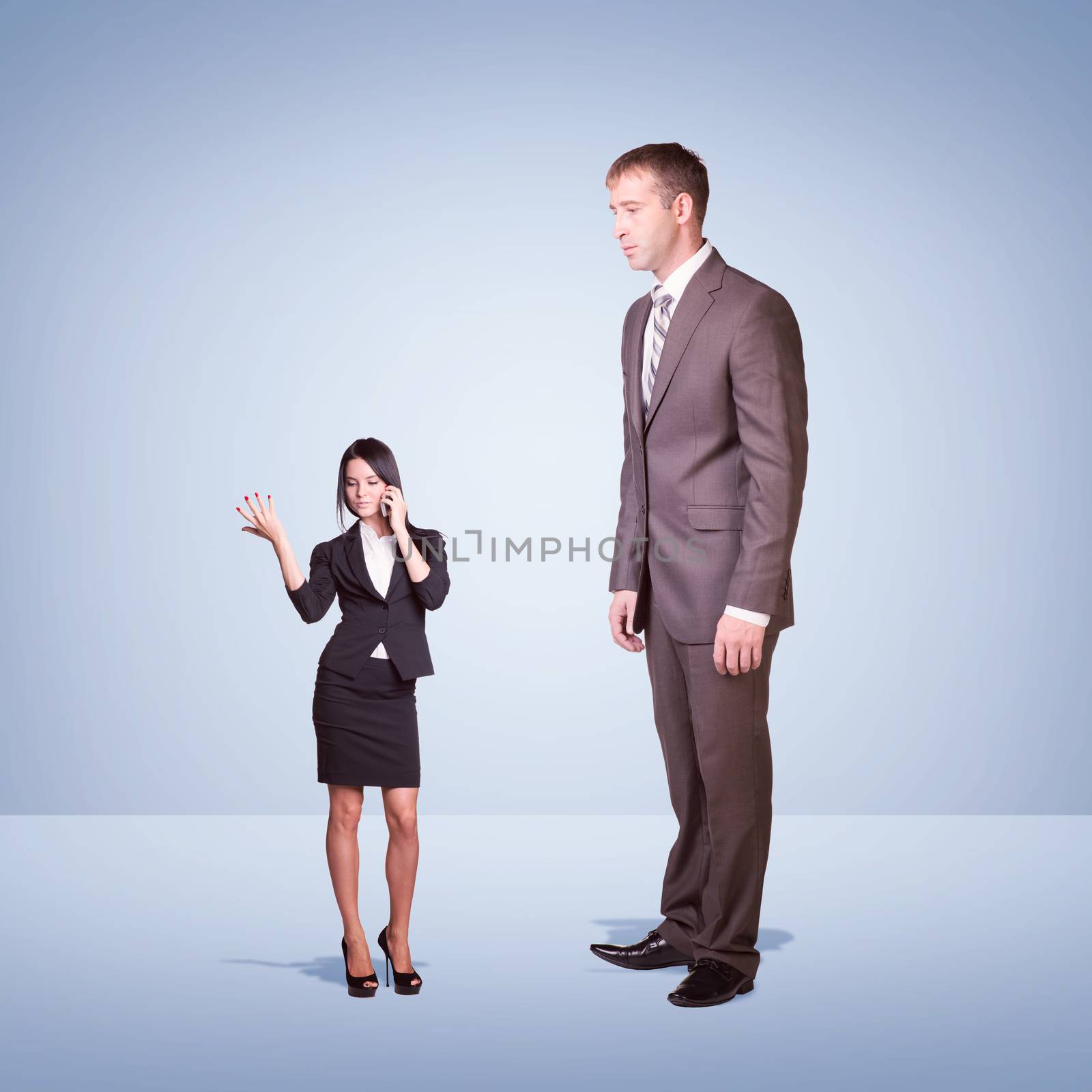 High businessman looking down at little woman using phone by cherezoff