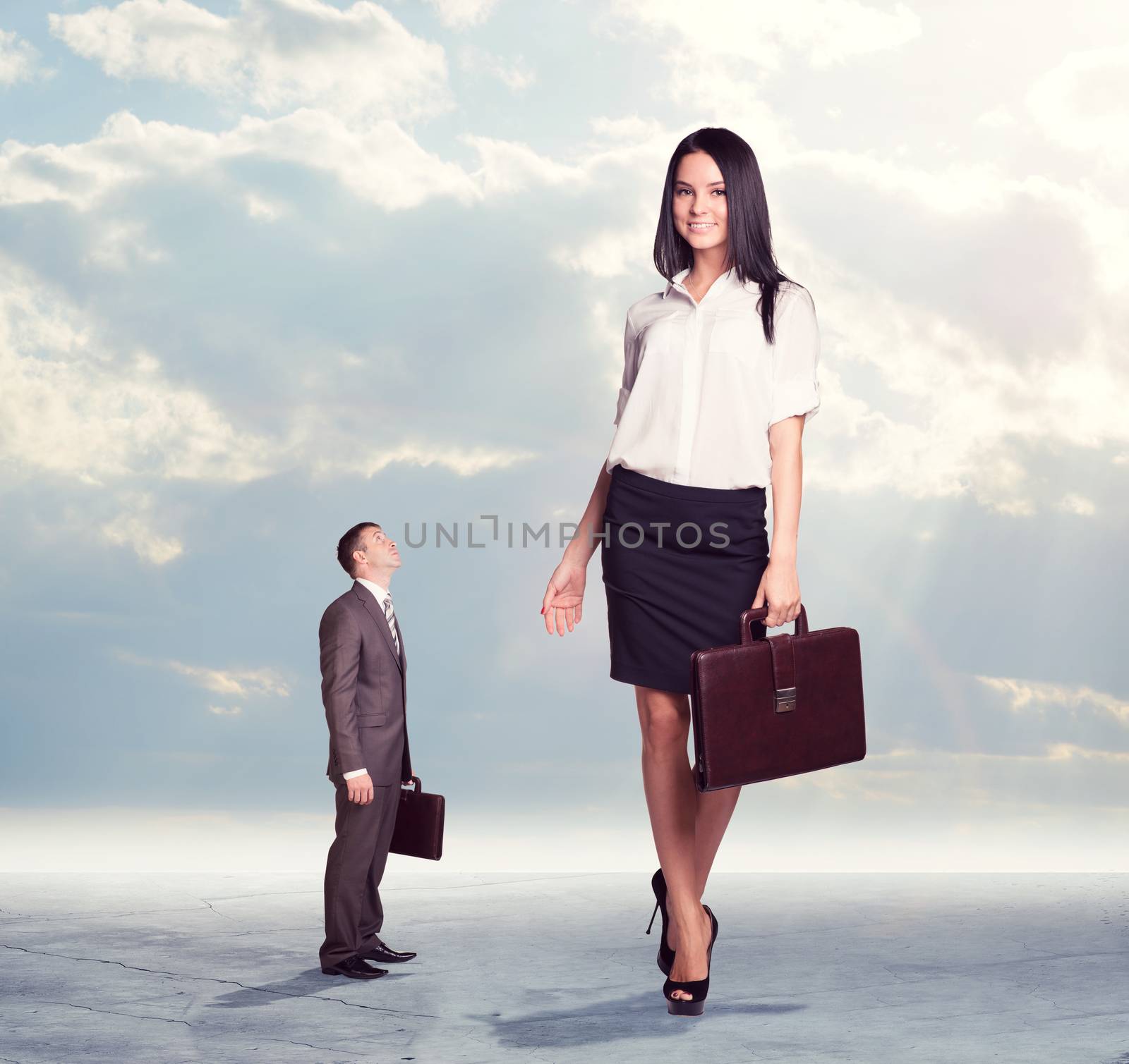 Small businessman looking up at on high walking businesswoman. Clouds and cement surface as background. Business concept